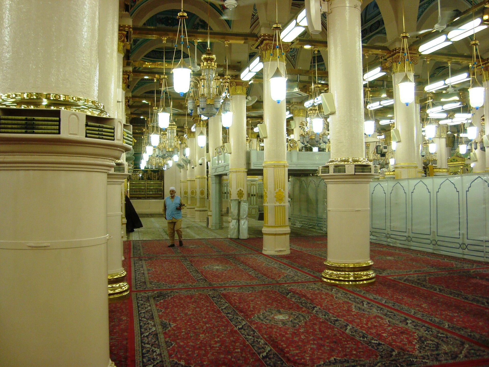 Interior prayer hall of the Prophet's Mosque in Medina with white columns, chandeliers and red prayer carpets