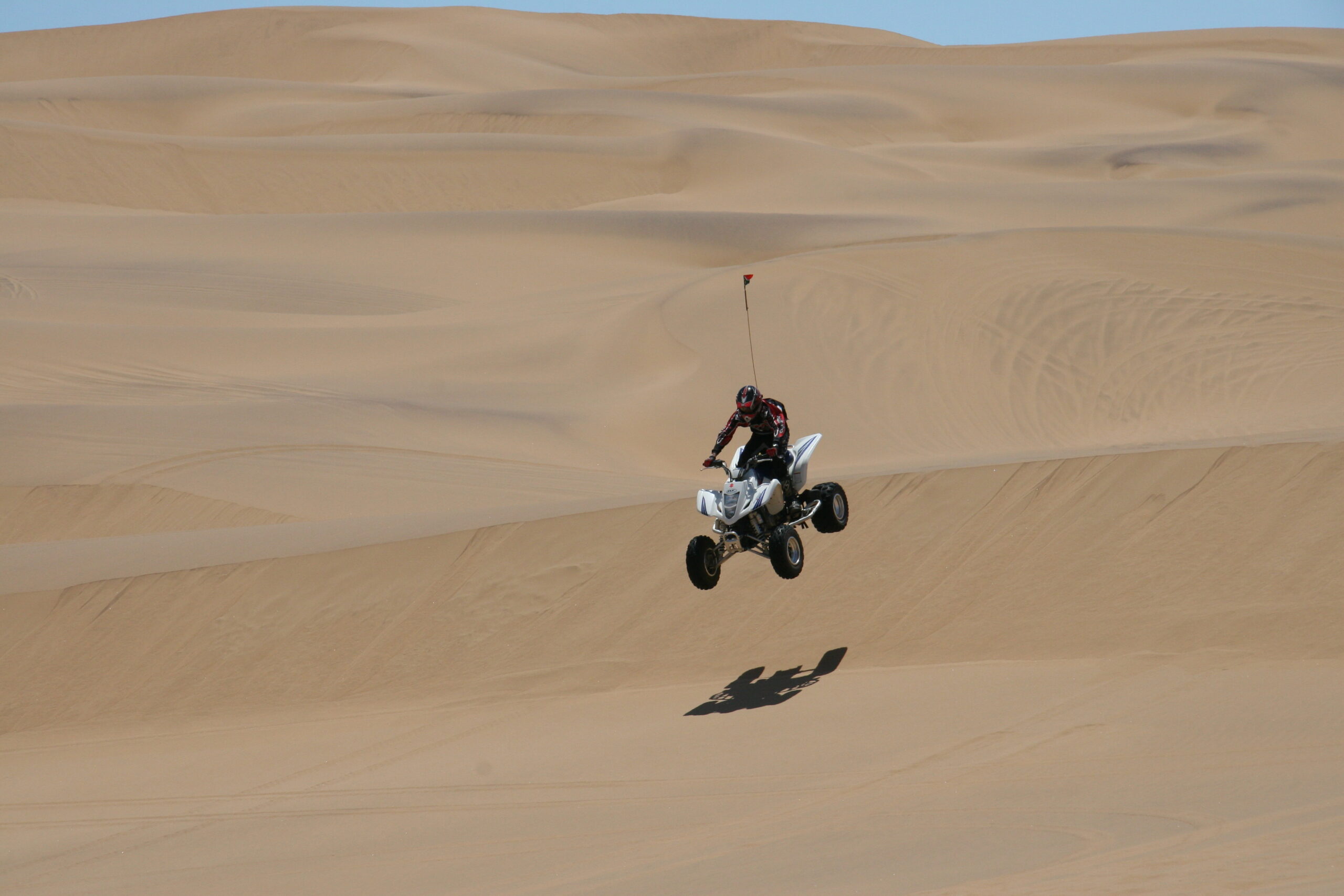 Quad bike launching over a sand dune crest in the desert