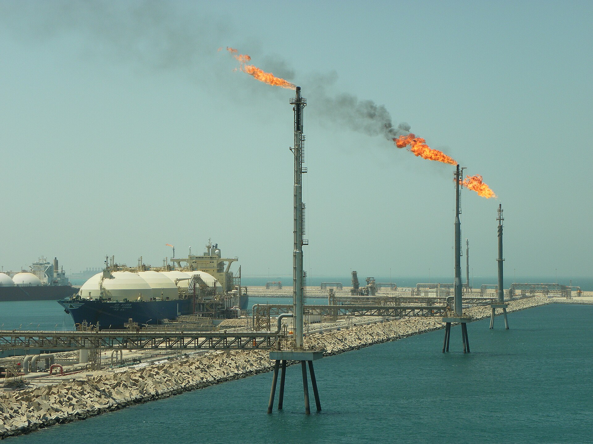 Ras Laffan LNG terminal, Qatar, with gas flare stacks burning and LNG tanker docked at the facility