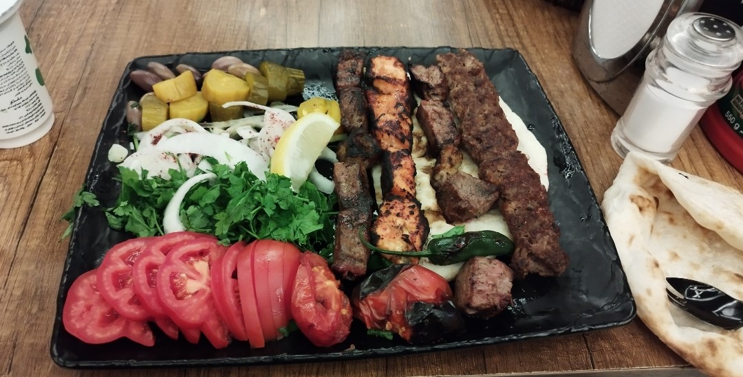 Mixed grill platter with kebab, tikka, fresh tomatoes, herbs, pickles, and flatbread