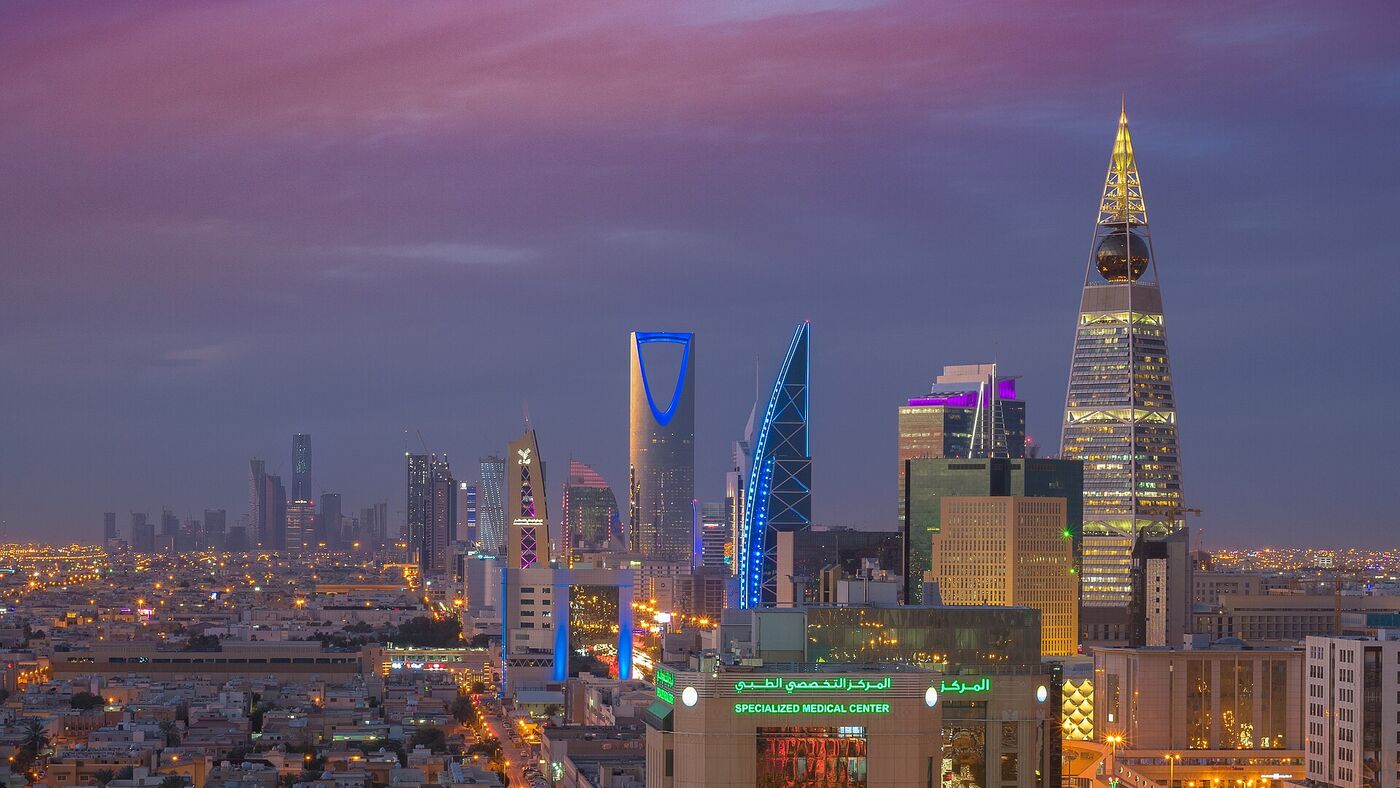 Riyadh skyline at night showing Kingdom Tower and Al Faisaliah Centre illuminated against a purple sky