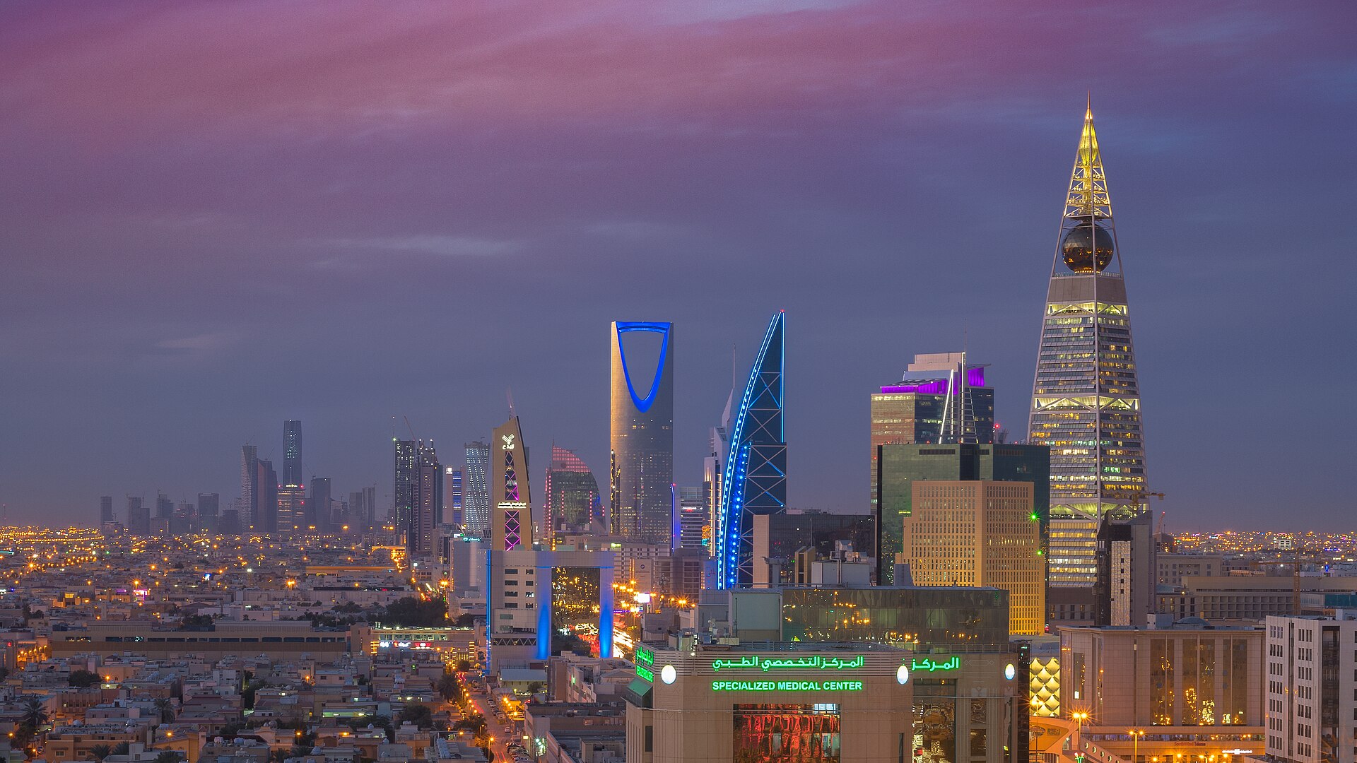 Riyadh skyline at dusk showing the Kingdom Centre tower and Al Faisaliah tower illuminated against a purple sky