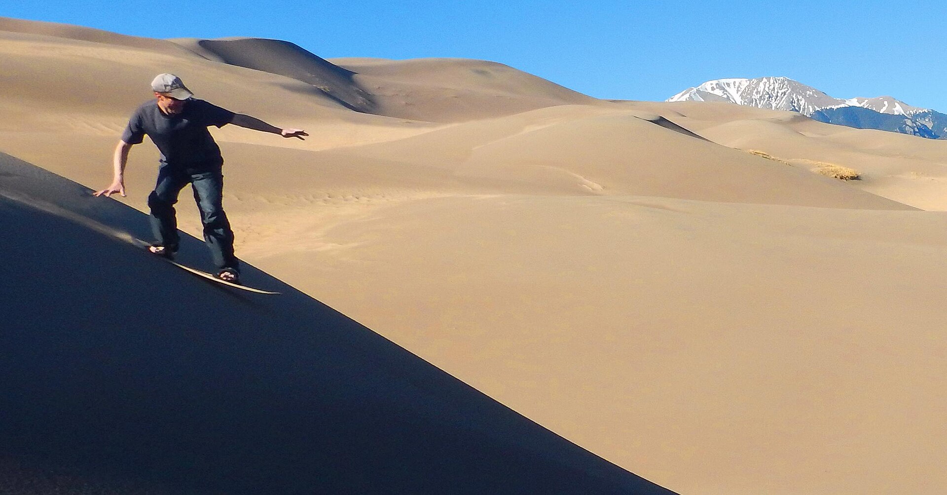 A sandboarder riding down a steep sand dune in the desert