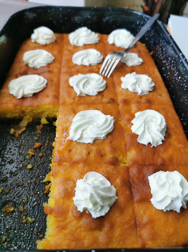 Basbousa semolina cake topped with whipped cream in a baking tray