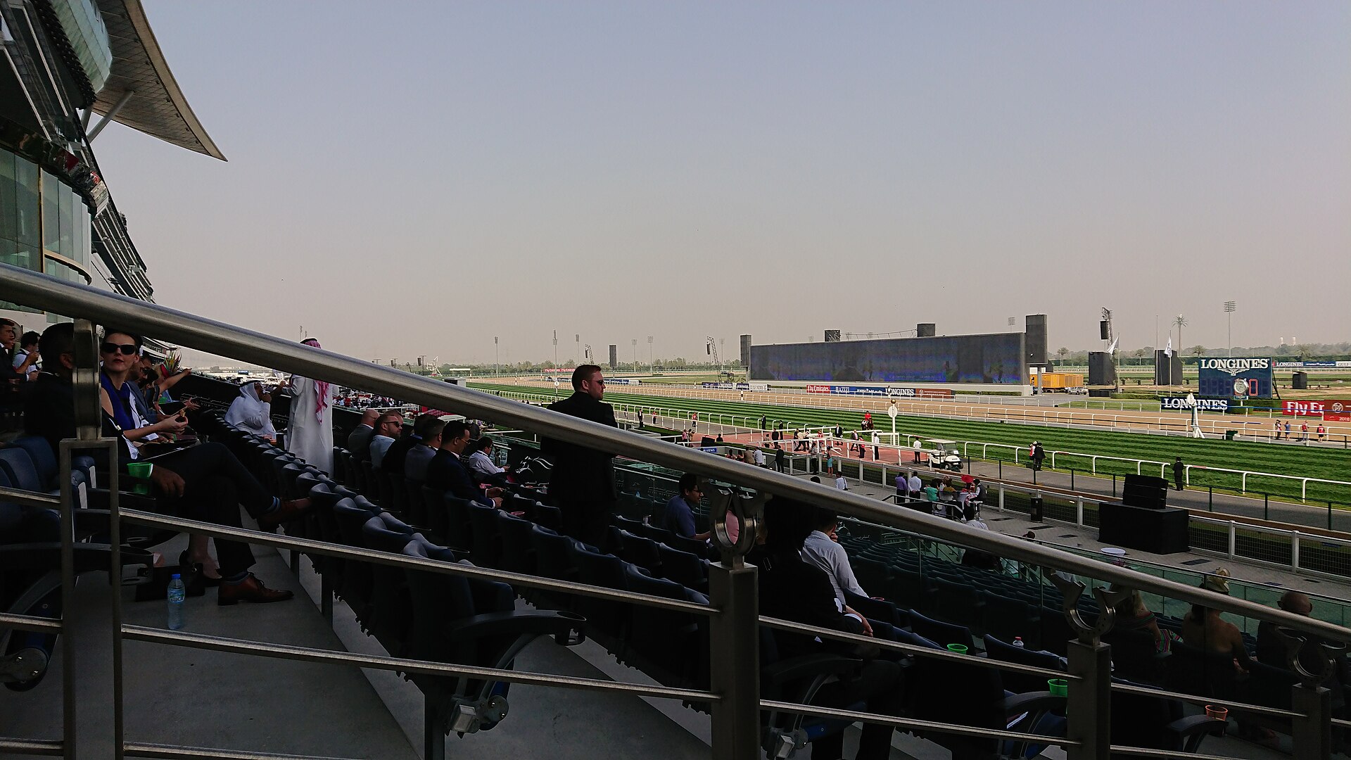 Grandstand view of a Gulf region racecourse with spectators watching horses on the dirt track