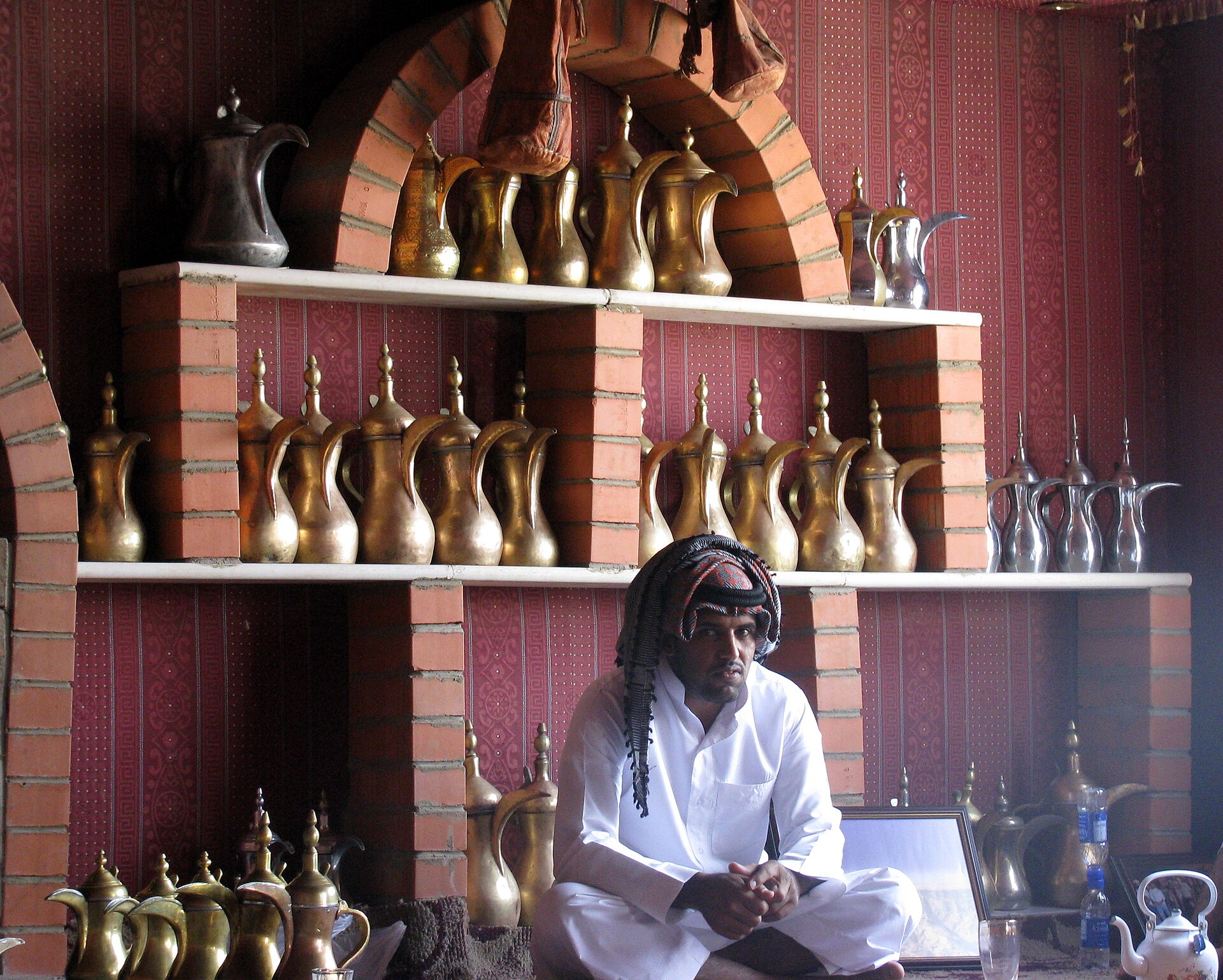 Brass and silver dallah coffee pots displayed on shelves in a traditional Saudi Arabian guest hall