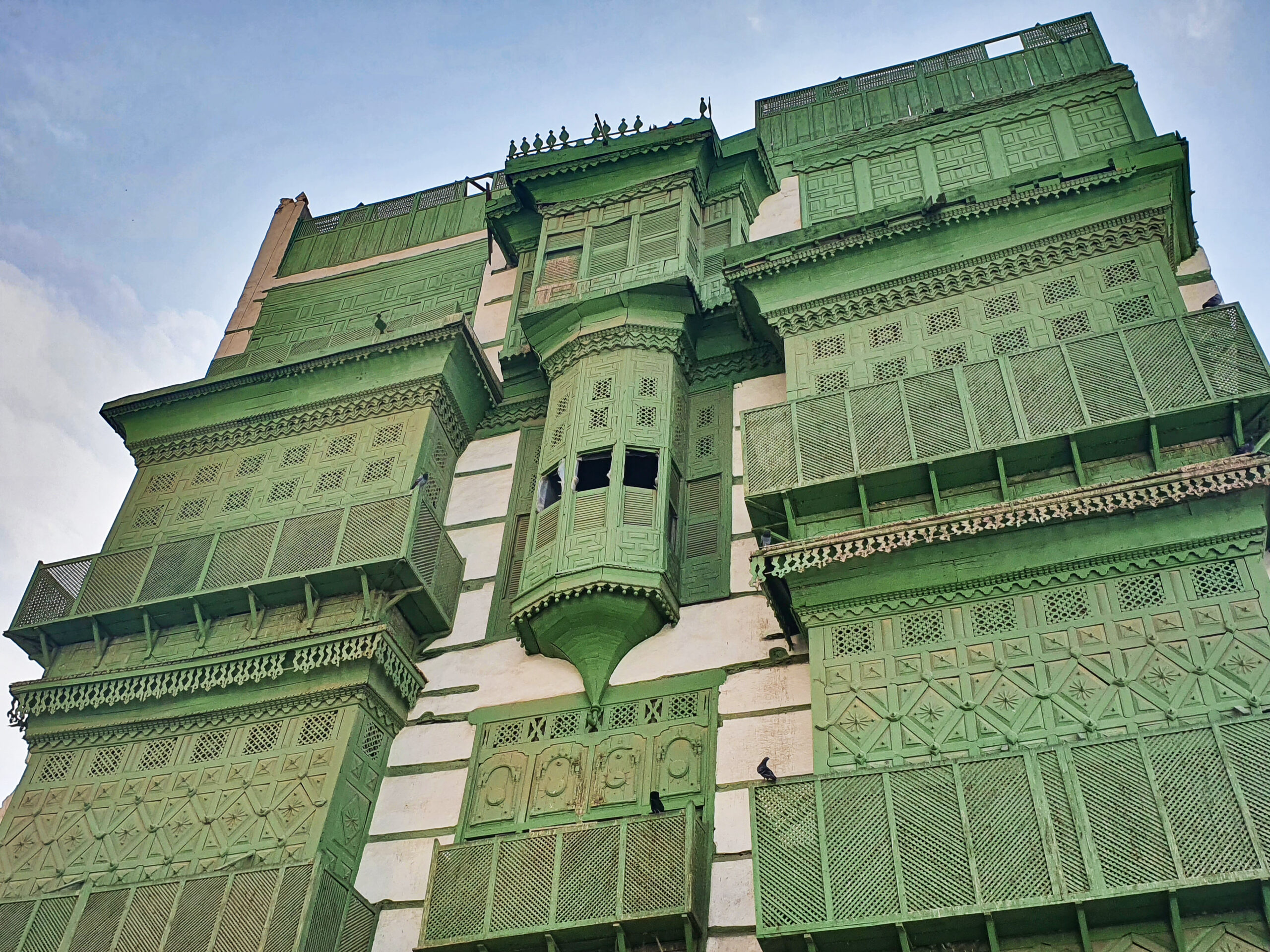 Traditional coral-stone building with green rawasheen wooden balconies in Al Balad historic district, Jeddah, Saudi Arabia