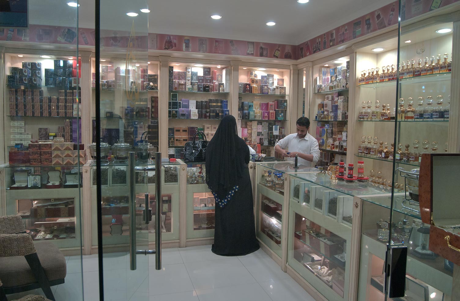 A woman in traditional dress browsing perfume bottles at a traditional Gulf souq stall
