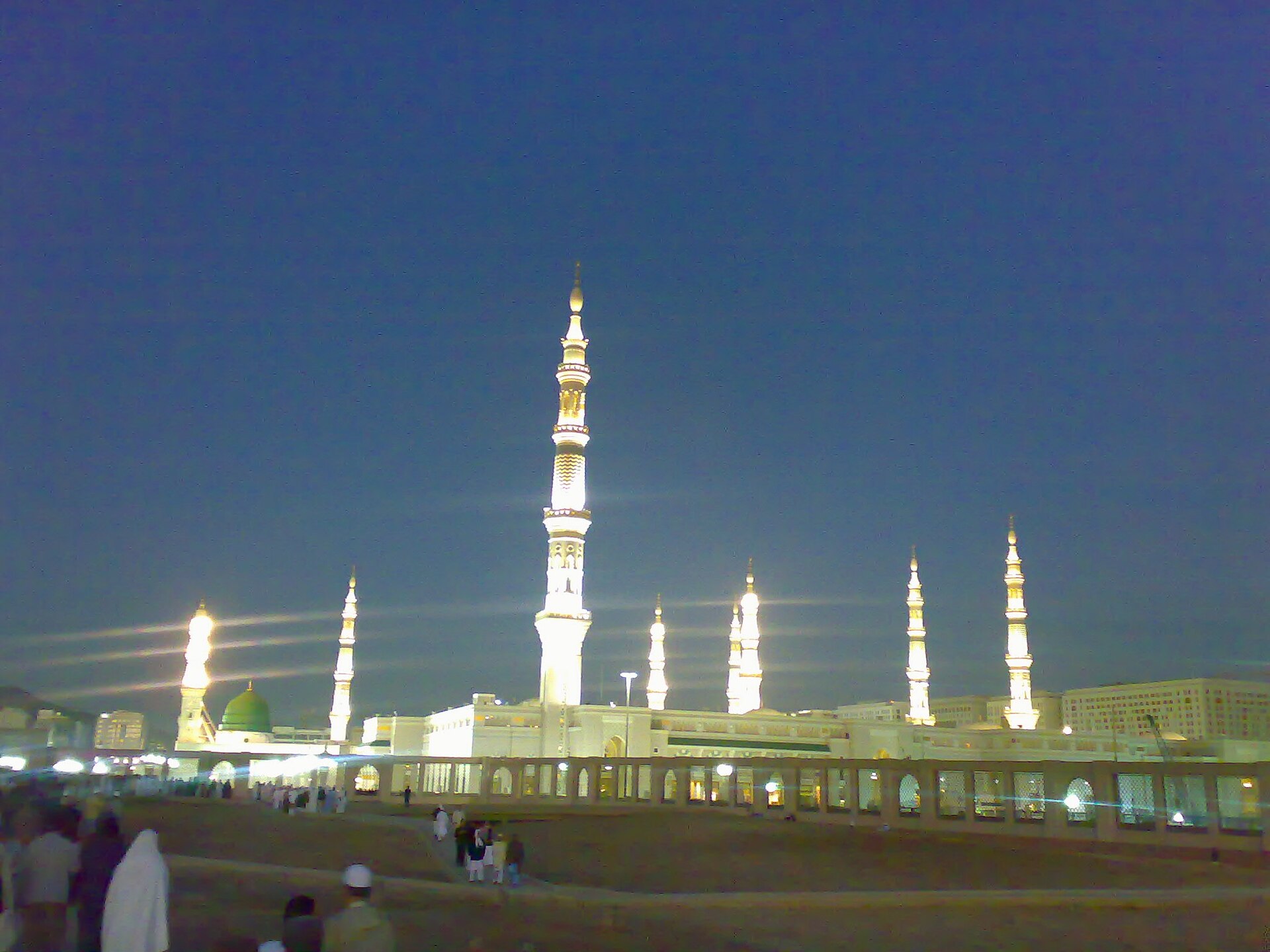 The Prophet's Mosque (Al-Masjid an-Nabawi) in Medina illuminated at dusk, with its distinctive minarets lit against a deep blue sky