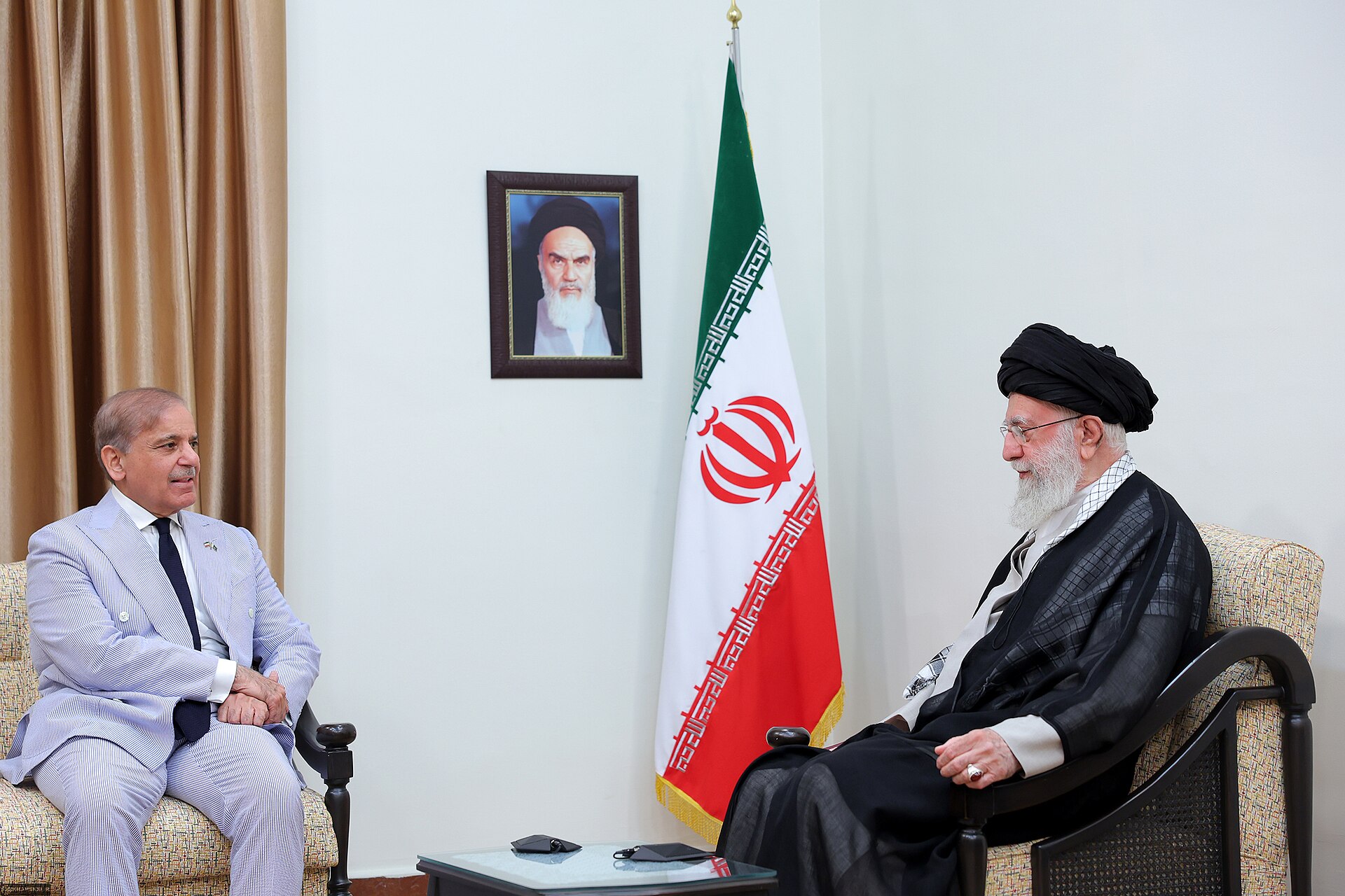 Pakistani Prime Minister Shehbaz Sharif seated across from Iranian Supreme Leader Khamenei in Tehran diplomatic meeting, Iranian flag between them
