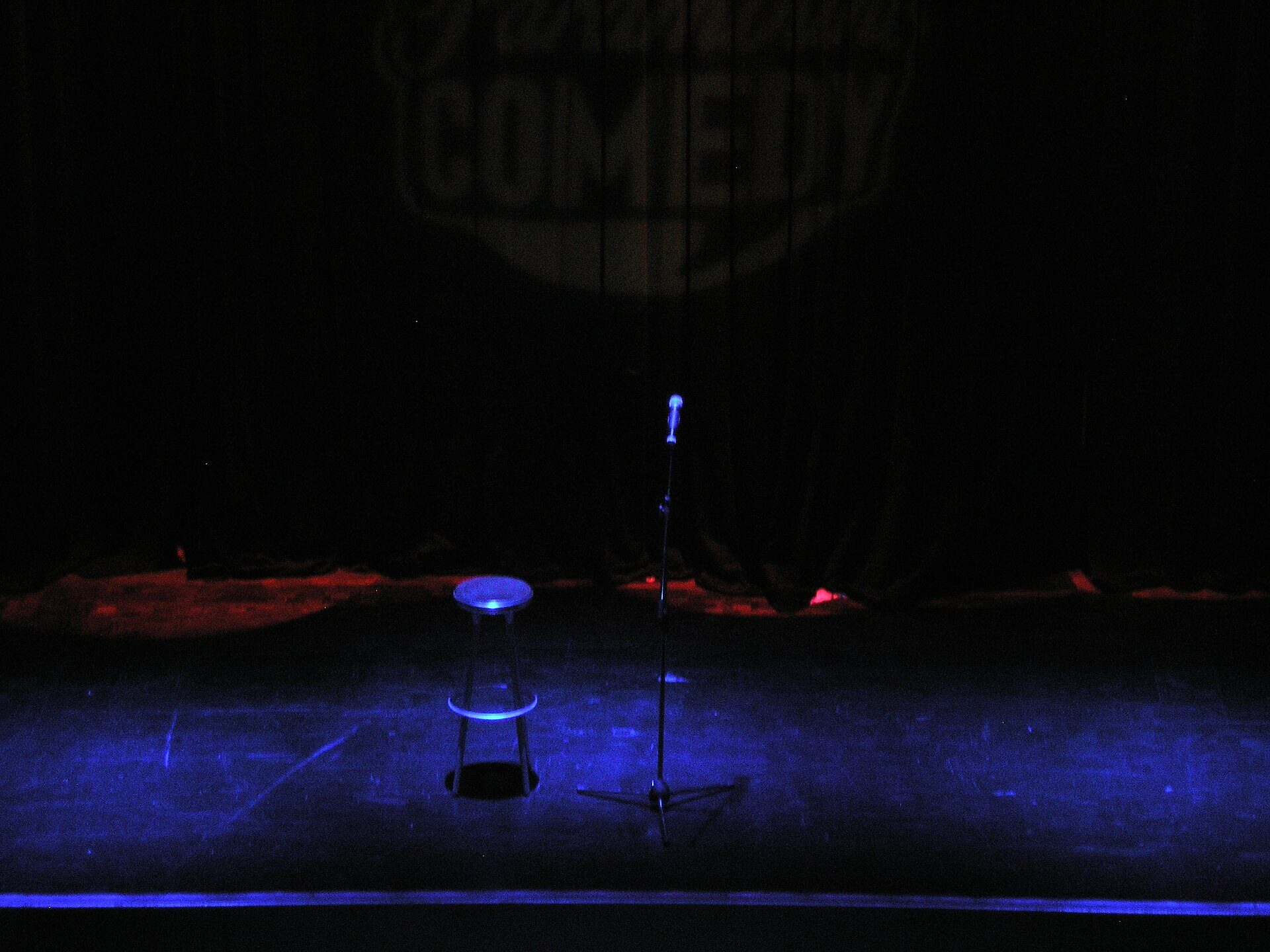 Stand-up comedy stage with a microphone and stool under blue stage lighting