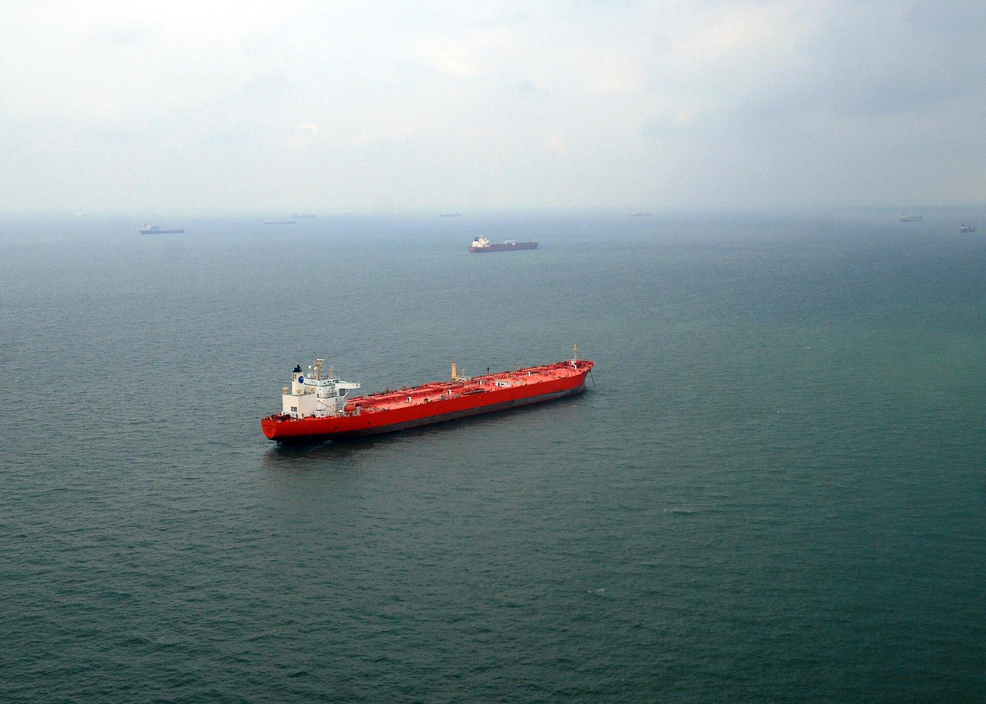 Multiple merchant ships and oil tankers anchored at sea waiting for port access, viewed from aerial perspective