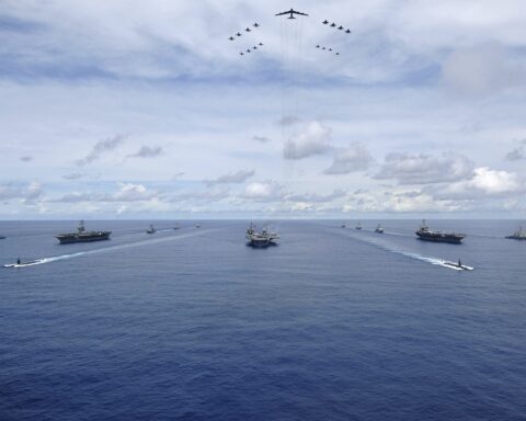 Three US Navy carrier strike groups — USS Nimitz, USS Kitty Hawk, USS John C. Stennis — in formation with B-52 bomber and fighter aircraft overhead during Valiant Shield 2007