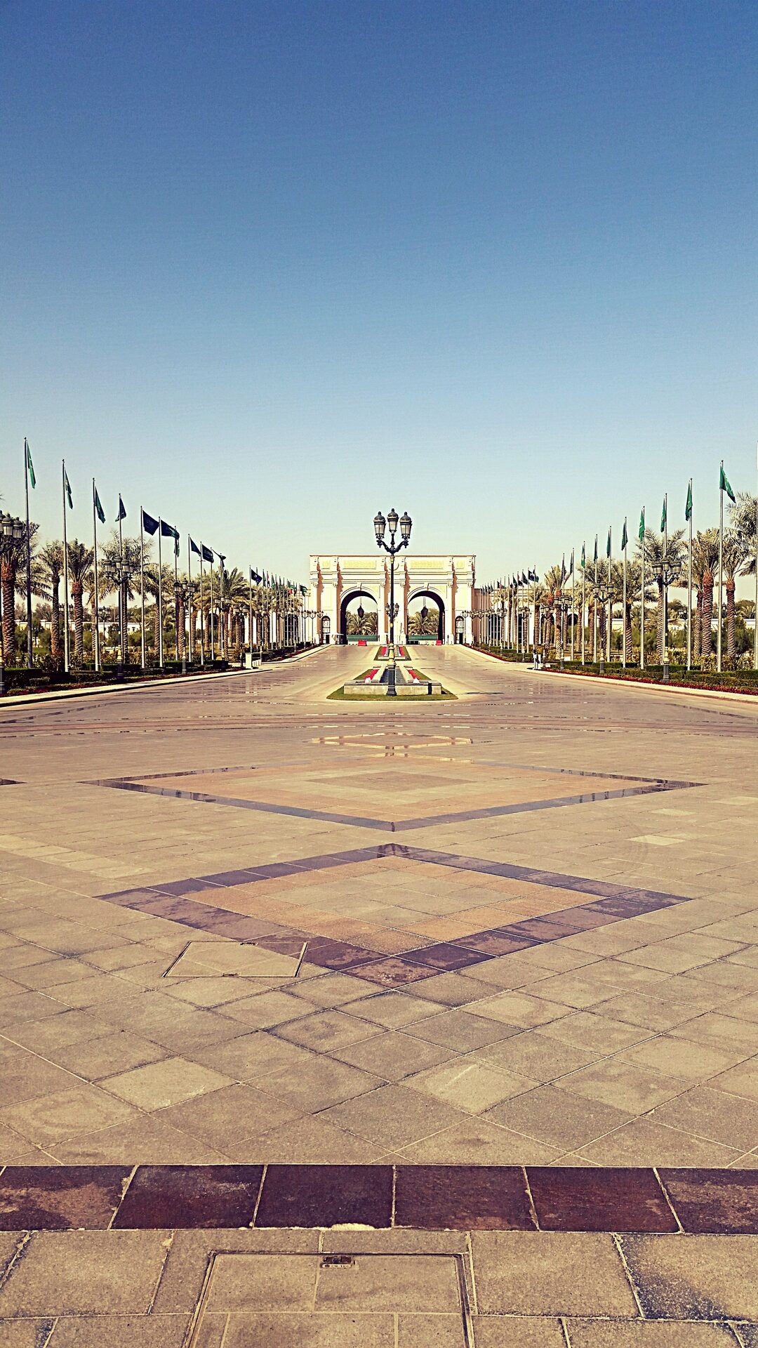 The grand entrance driveway of the Ritz-Carlton Riyadh, lined with palm trees and Saudi flags