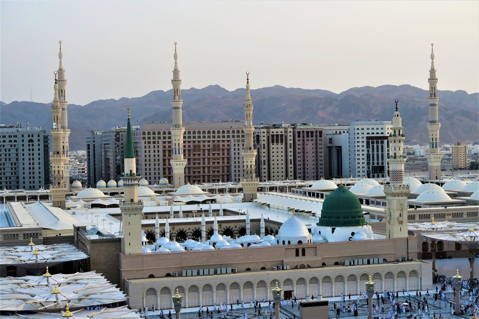 Bird's eye view of Al-Masjid an-Nabawi in Medina with the iconic Green Dome, minarets, and surrounding hotel towers