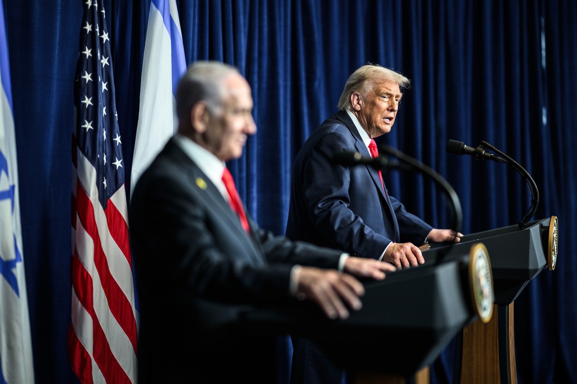 US President Donald Trump and Israeli Prime Minister Benjamin Netanyahu at joint press conference podiums with American and Israeli flags, White House, December 2025
