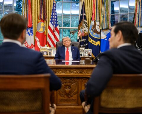 President Trump seated at the Resolute Desk in the Oval Office with Vice President JD Vance and Secretary of State Marco Rubio, the national security team directing simultaneous threats and diplomacy toward Iran in April 2026