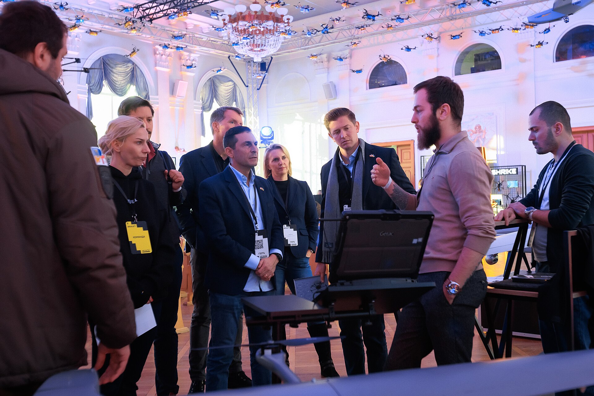 Inside a Ukrainian defense industry exhibition, with drone and weapons hardware visible, as US officials from the Defense Innovation Unit and Ambassador Nate Fick review Ukrainian military technology in Kyiv
