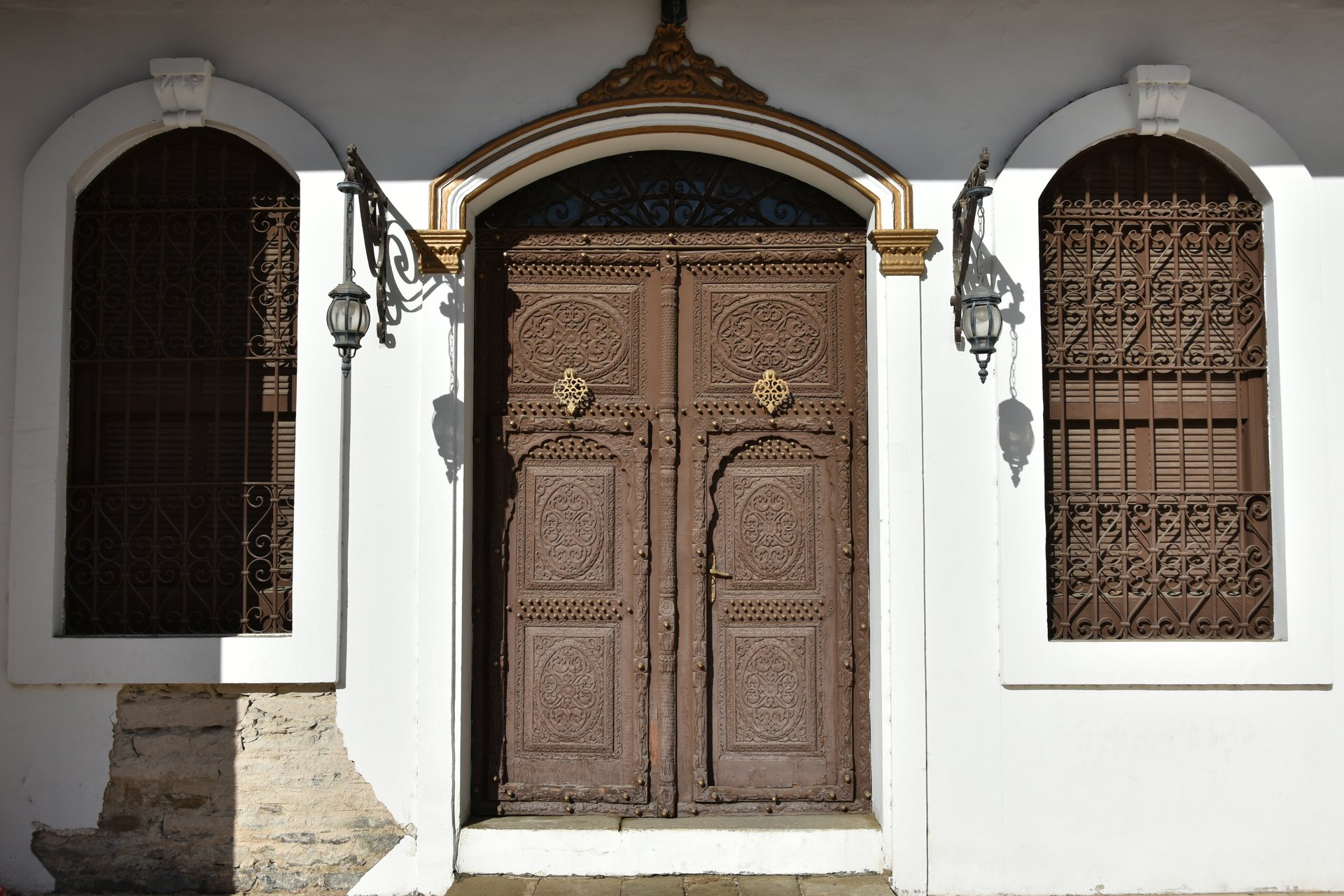 Ornate carved wooden doors and arched iron-grille windows at the entrance of Shubra Palace in Taif, Saudi Arabia