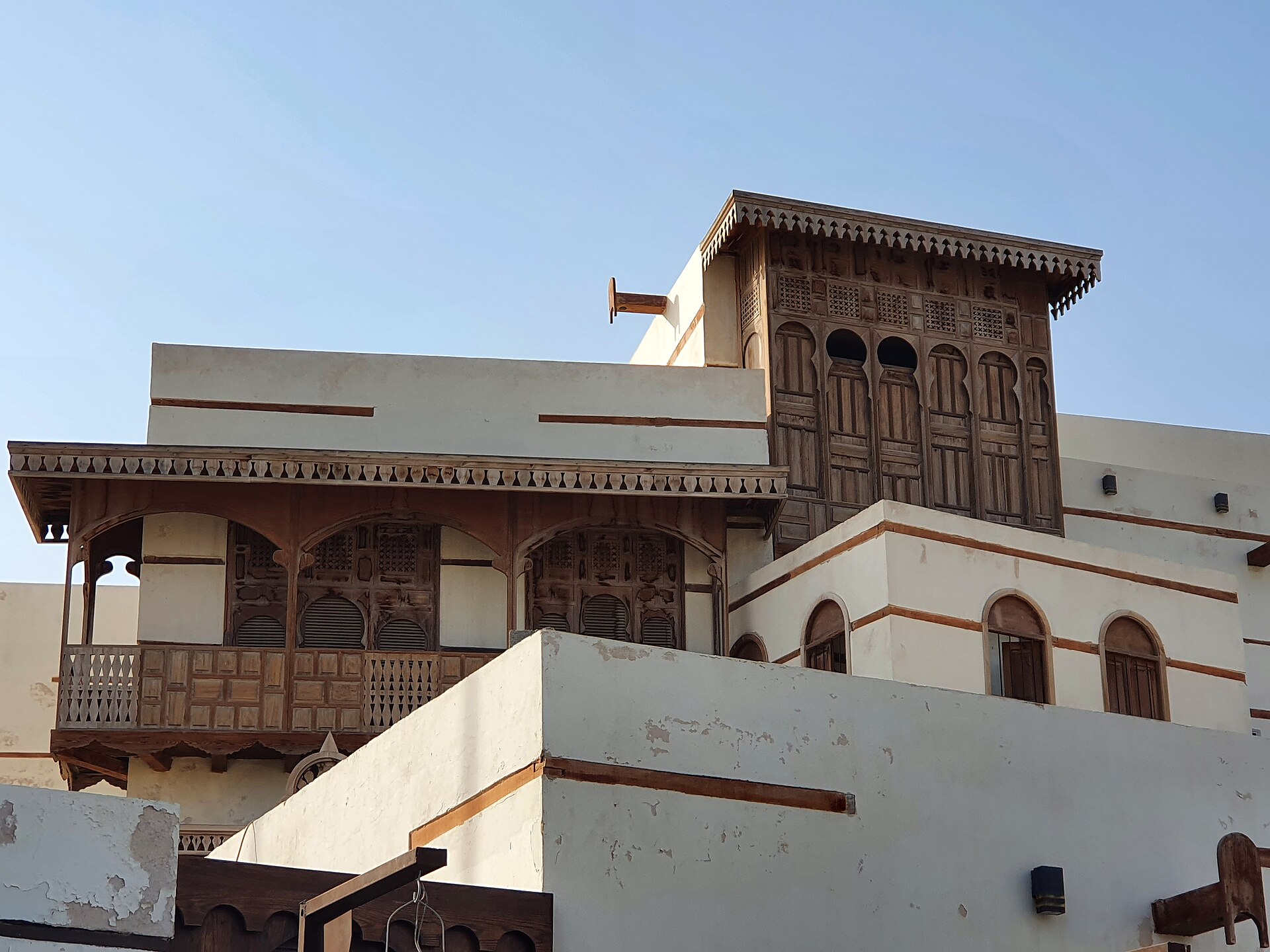 Detail view of a traditional coral-stone house in Yanbu's historic quarter with ornate wooden upper balconies and lattice screens