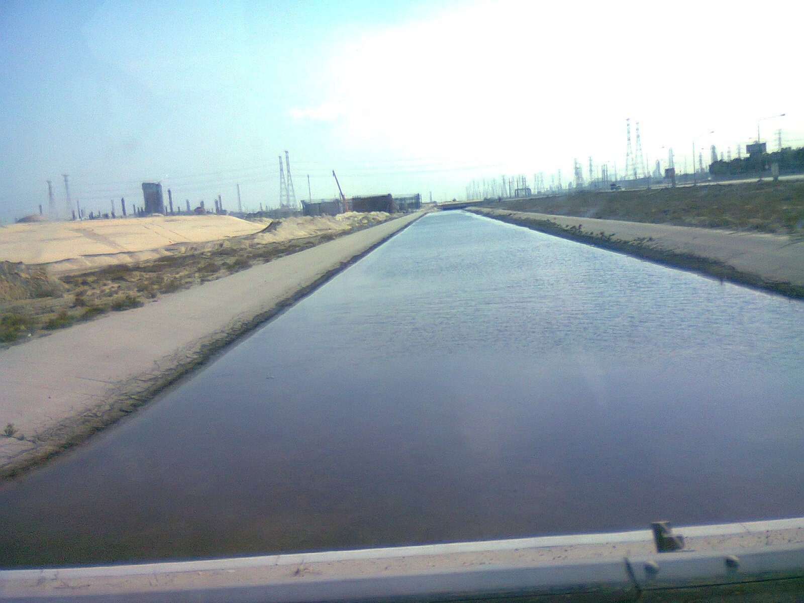 Jubail Industrial City showing a water canal stretching into the distance with industrial chimneys and transmission towers on the horizon