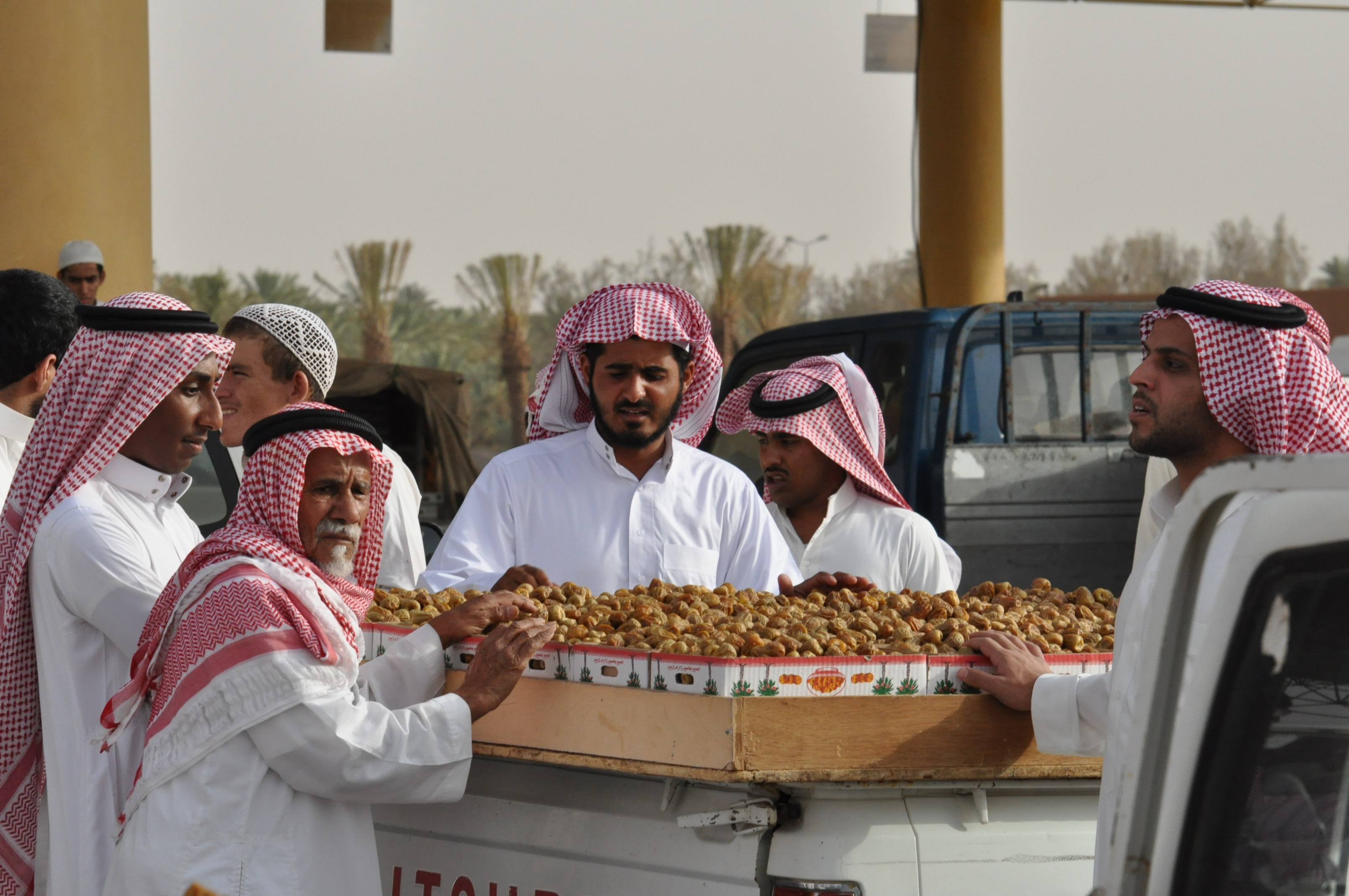 Traders in traditional Saudi dress displaying trays of fresh dates at the Buraydah Date Market