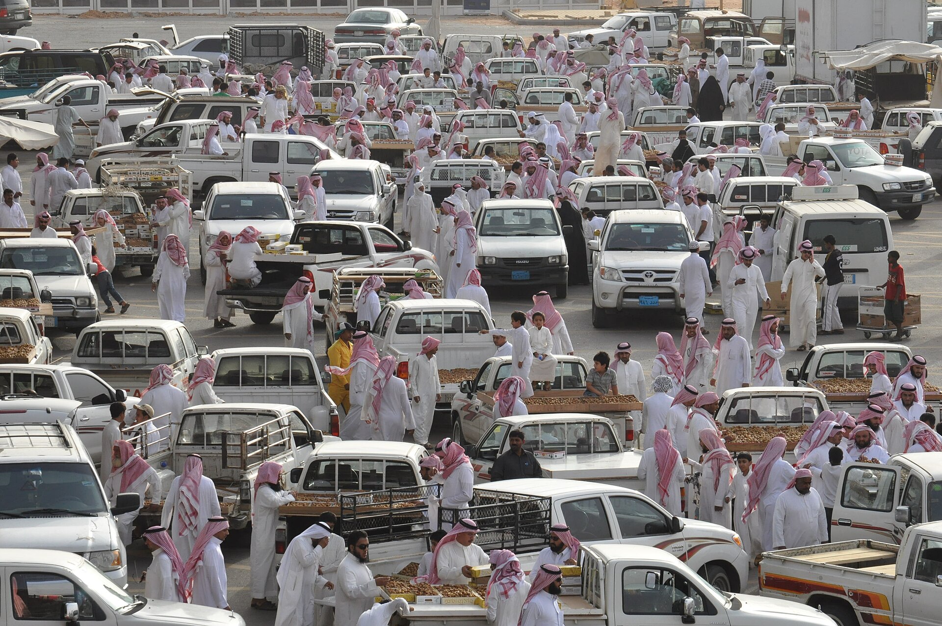 Aerial view of the bustling Buraydah Date Market with rows of pickup trucks loaded with dates and crowds of traders