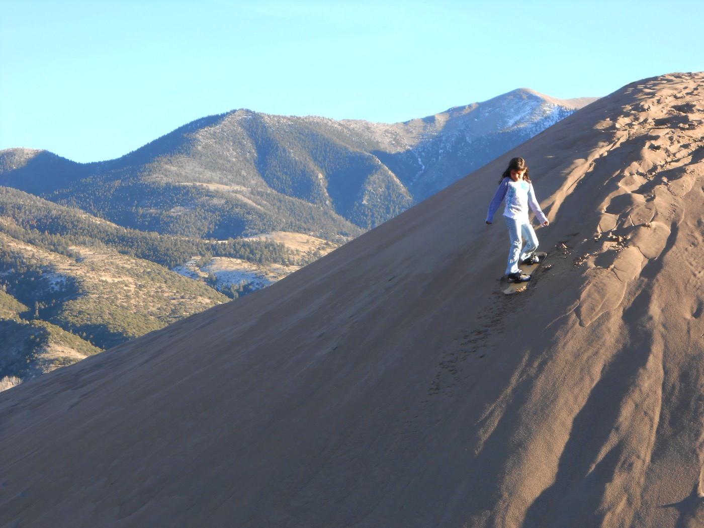 Person sandboarding down a steep desert sand dune