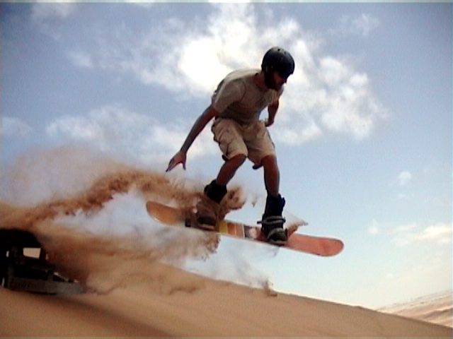 Sandboarder catching air on a desert sand dune