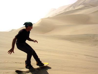Person lying prone on a sandboard descending a dune