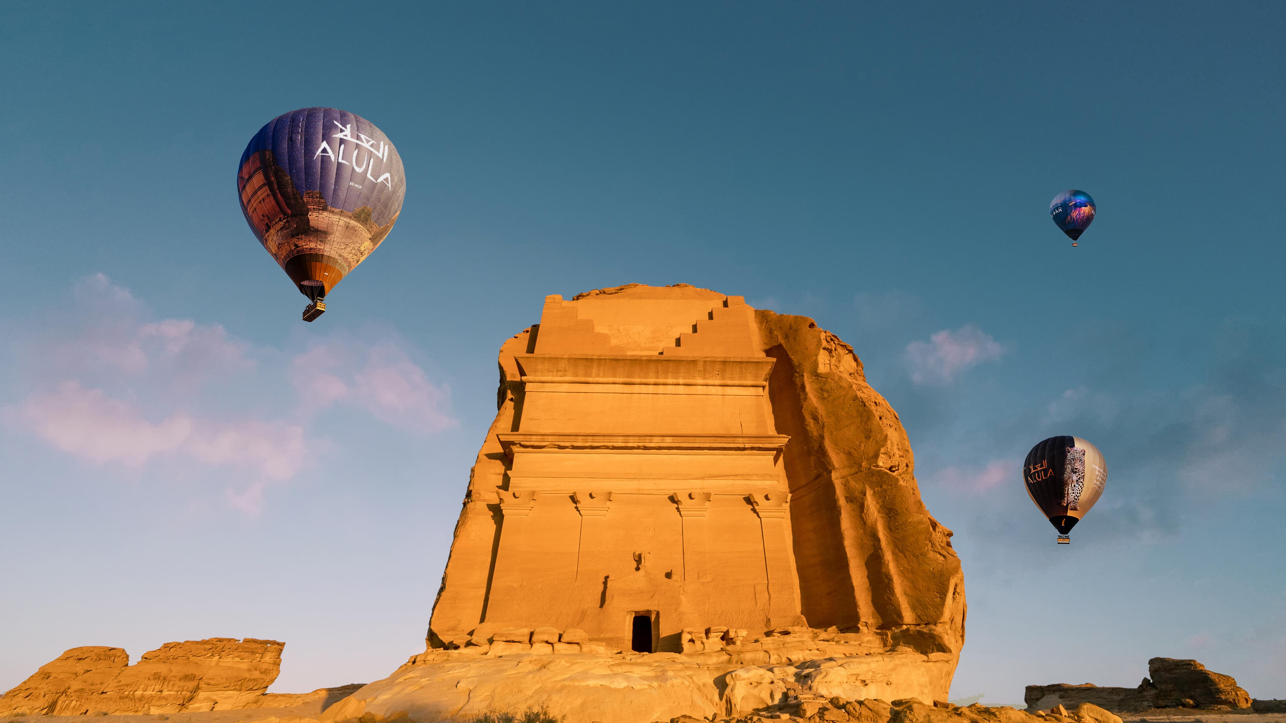 AlUla-branded hot air balloons floating near Qasr al-Farid, the Lonely Castle tomb, at golden hour