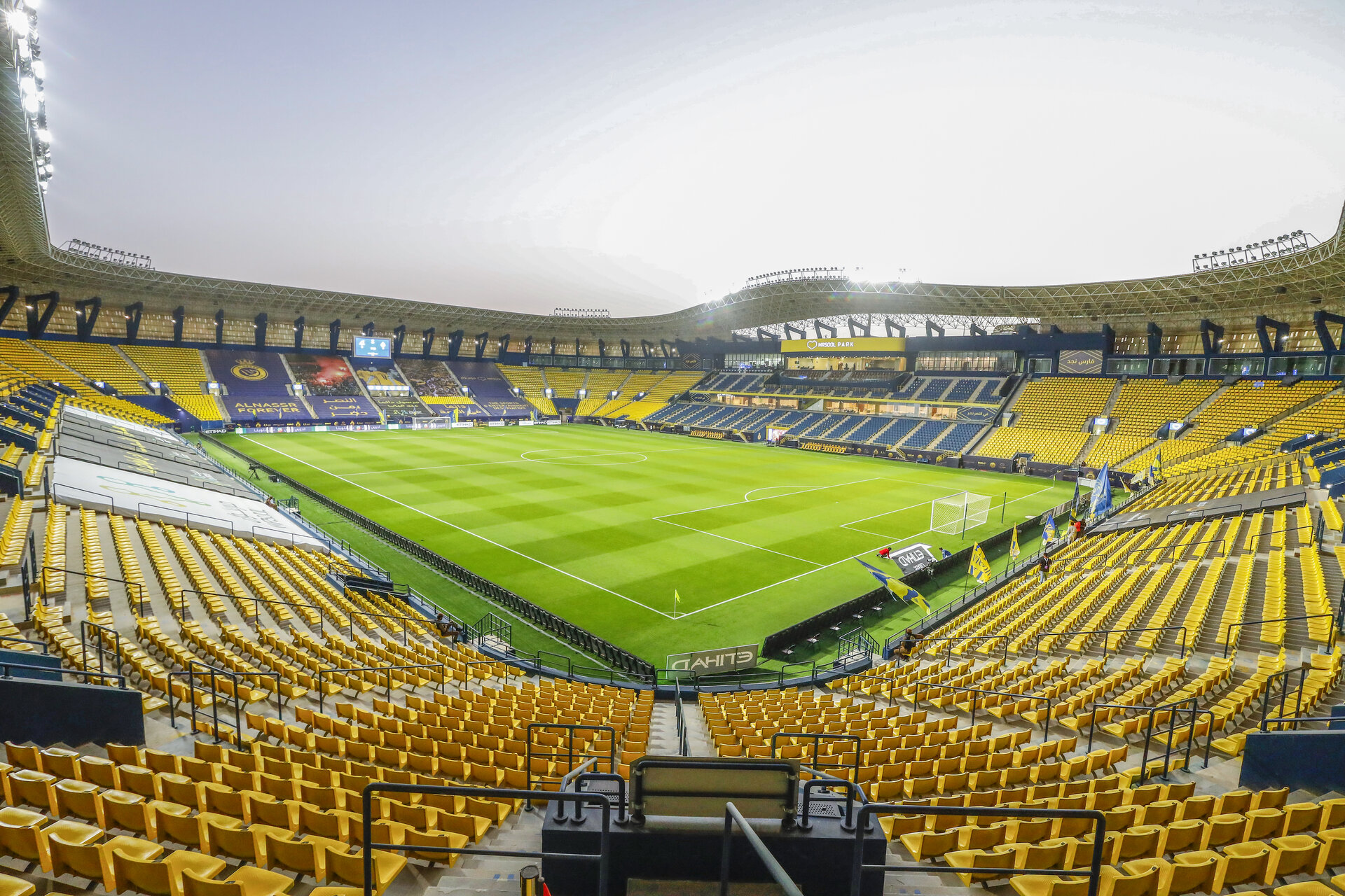 Exterior view of Al-Awwal Park stadium in Riyadh with yellow seats and floodlights, home of Al-Nassr FC