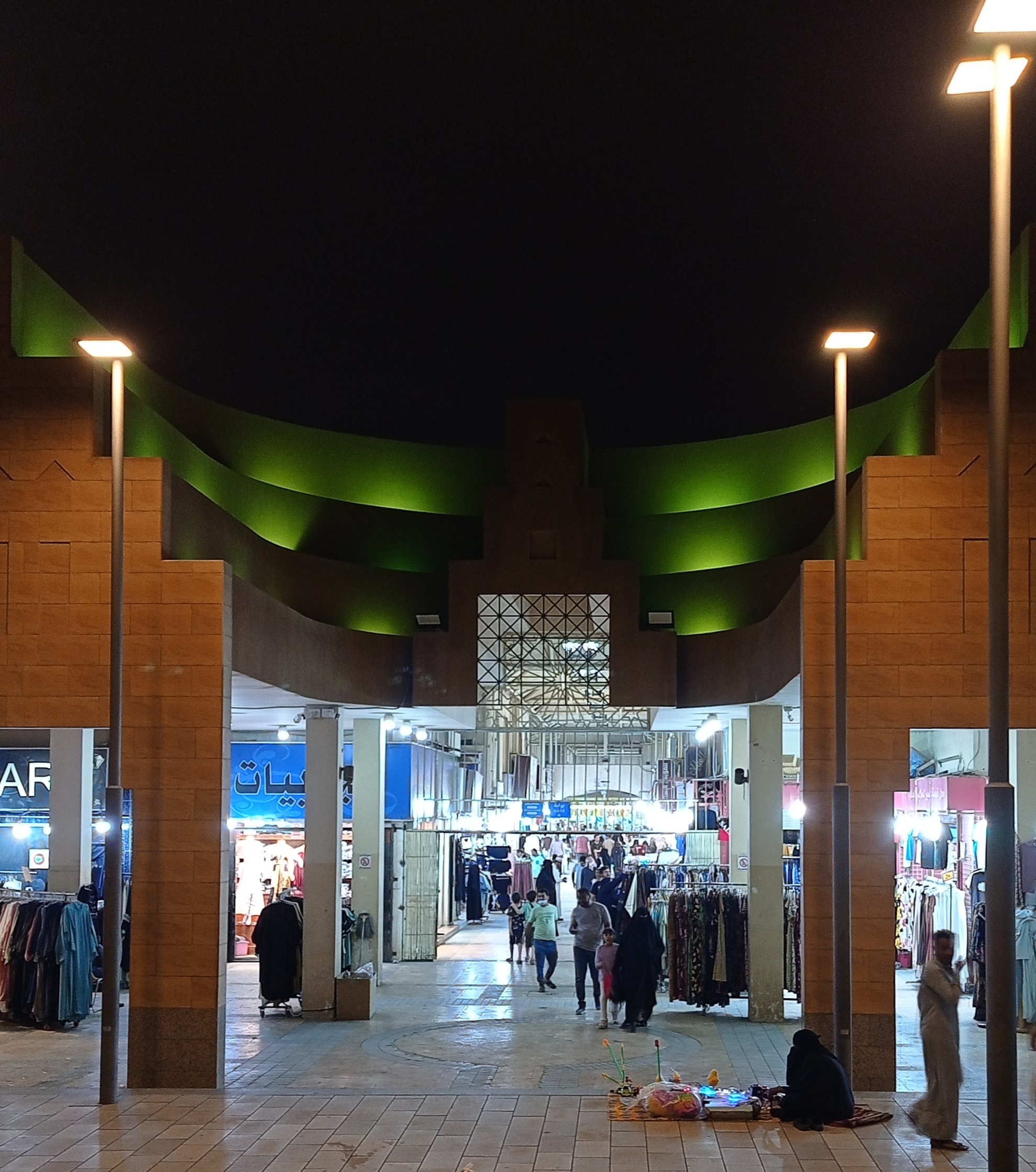 Arched gateway of a traditional Riyadh souq lit up at night, with stalls and shoppers visible through the passageway