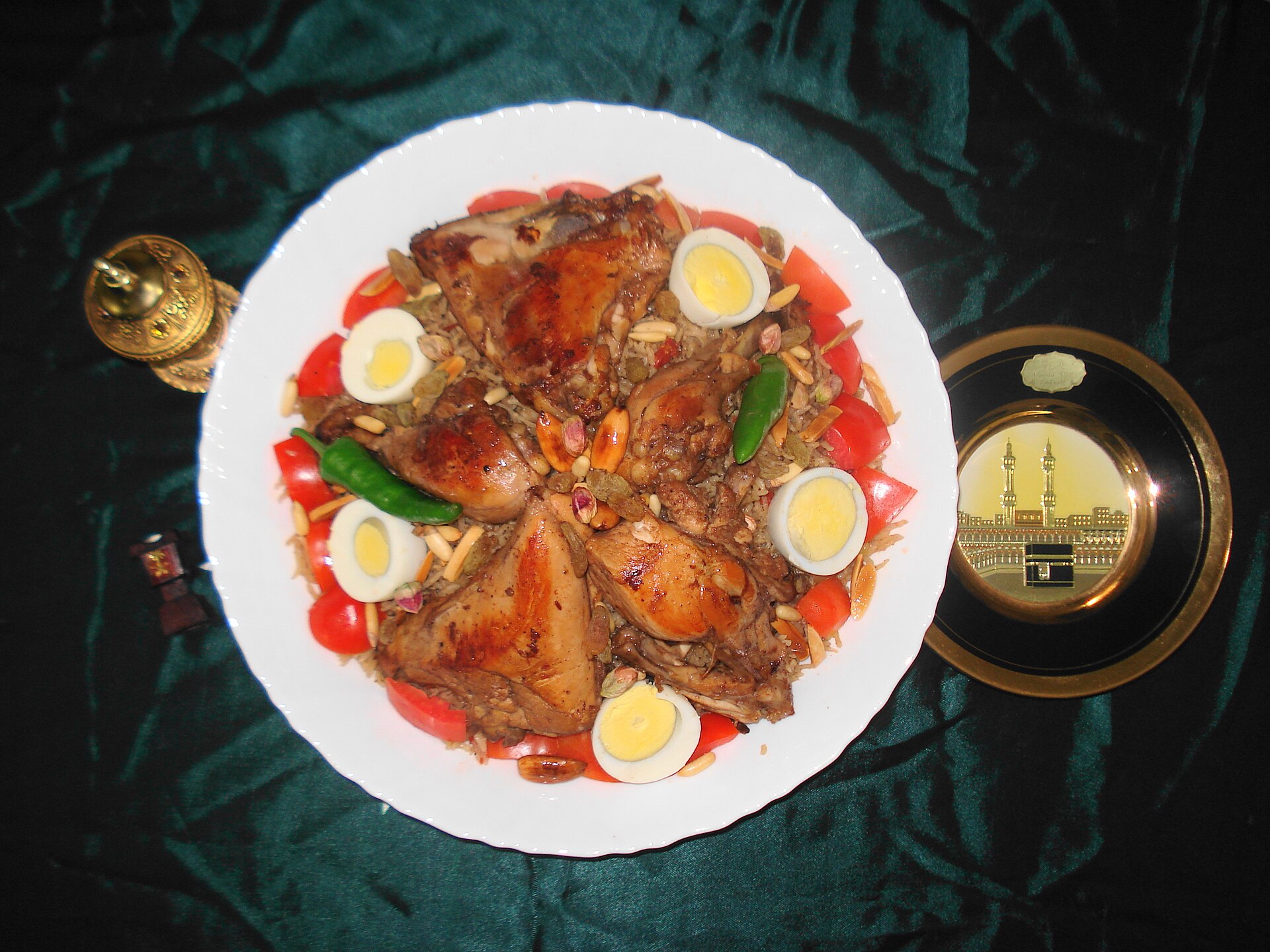 A decorated platter of chicken kabsa with quail eggs and pepper, alongside a traditional Arabic coffee pot