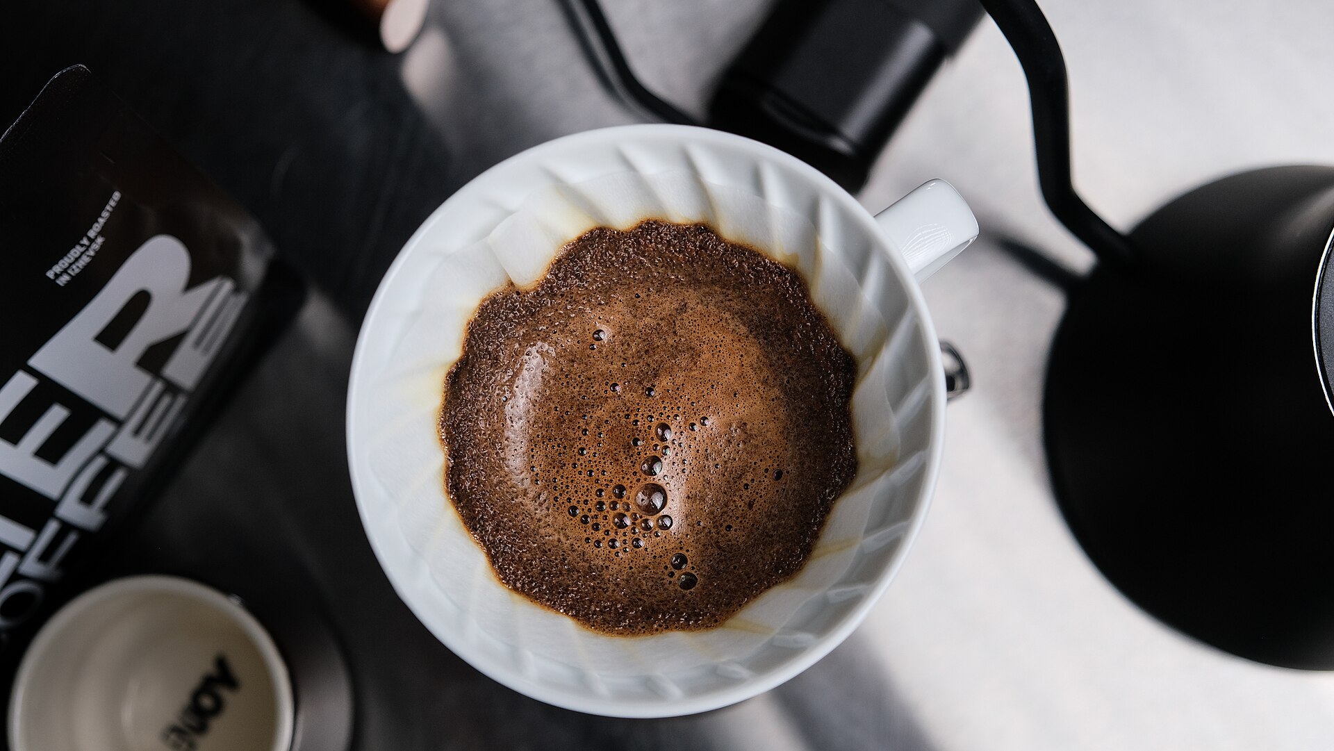 Pour over coffee brewing in a white V60 dripper with a black kettle