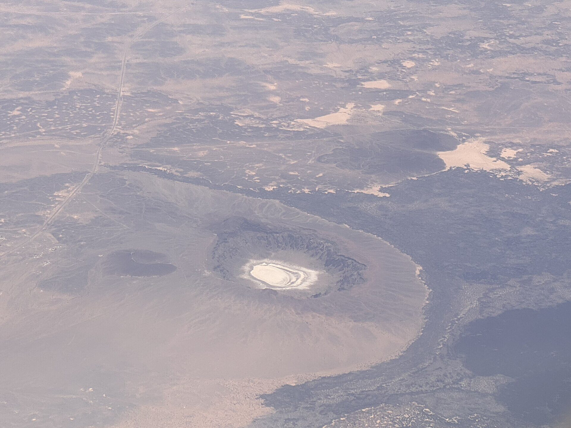 Aerial view of Al Wahbah Crater from an airplane showing the full circular formation and white salt floor against the dark Harrat Kishb lava field
