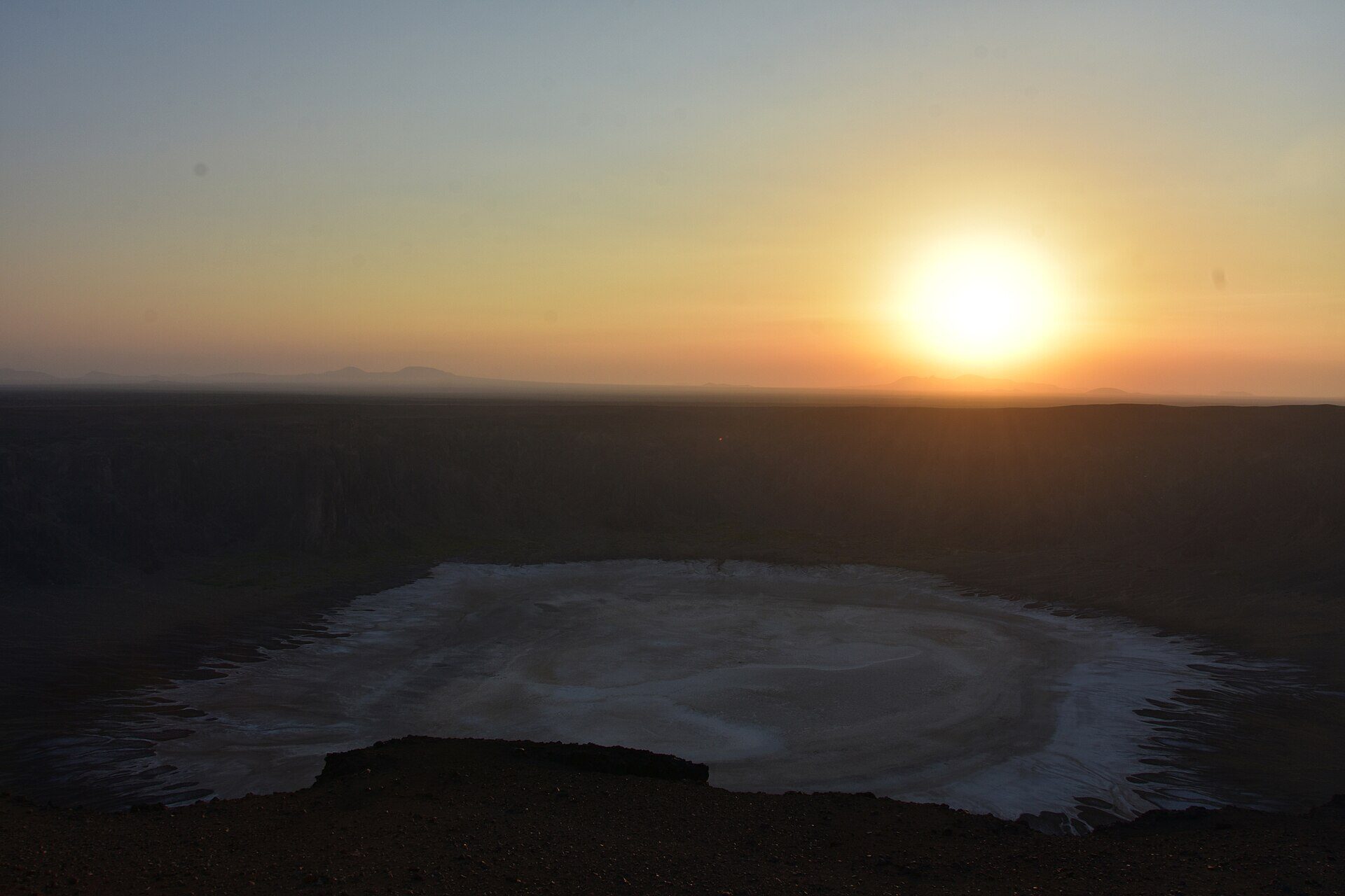 Al Wahbah Crater at sunrise with the white salt floor glowing beneath a golden sky