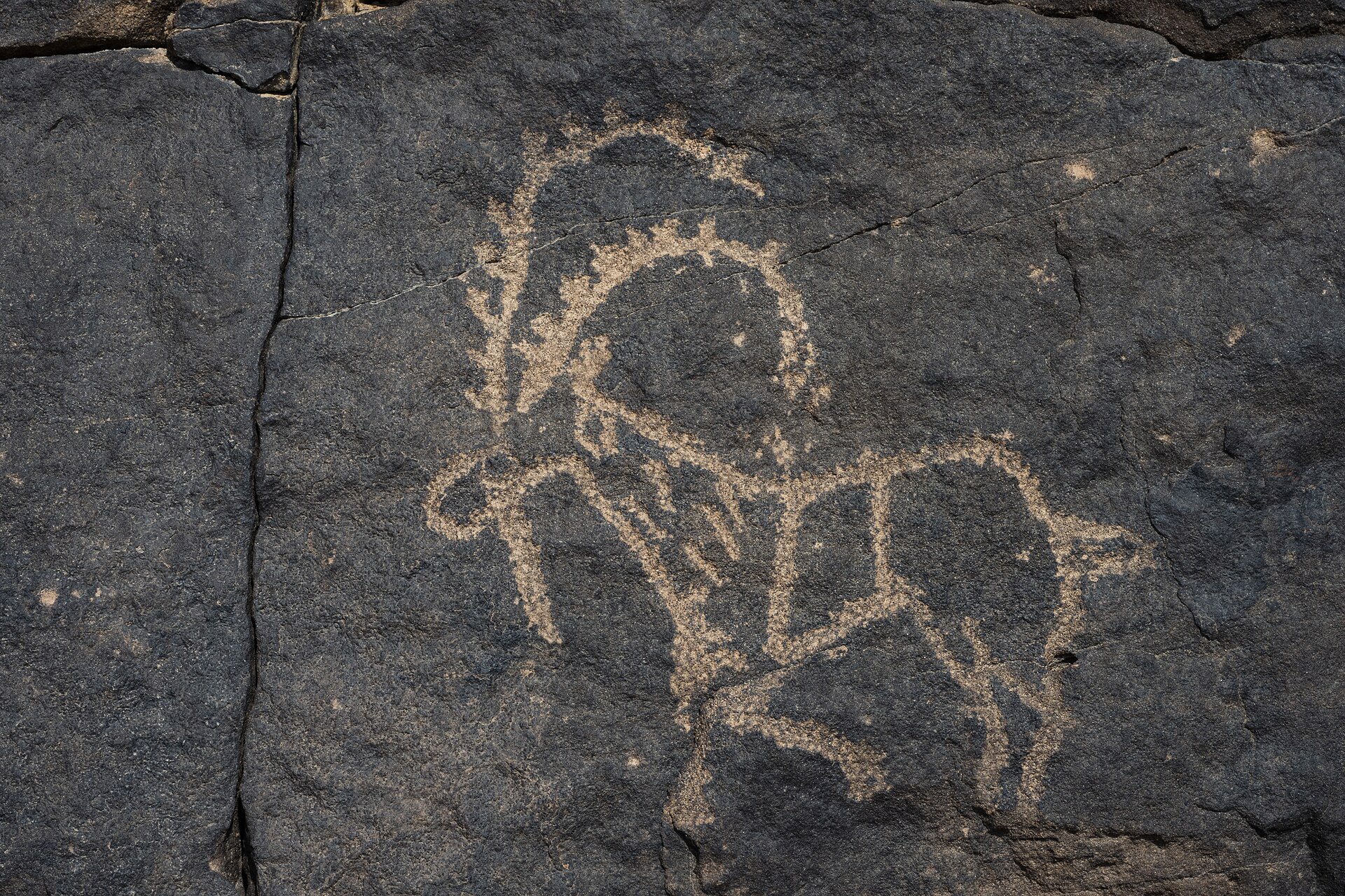 Ancient rock art petroglyph at Hima Cultural Area showing a human figure carved into dark sandstone