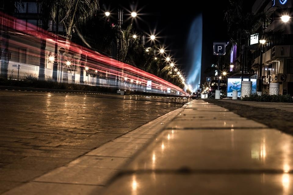 Jeddah Corniche at night with King Fahd's Fountain glowing in the background and light trails from passing traffic
