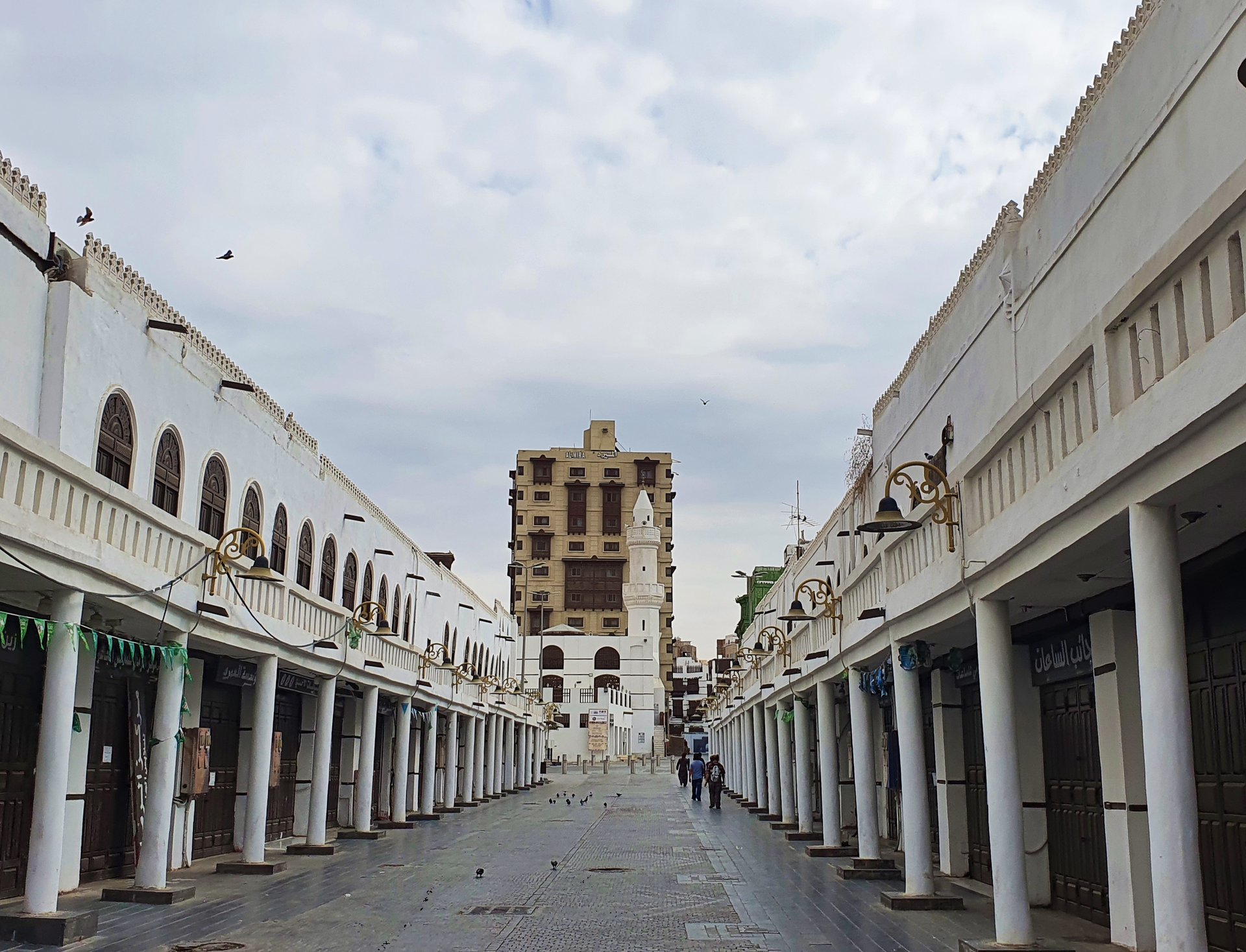 Market street in old Jeddah with al-Mimar Mosque in the background, showing the covered souk arcade with white colonnaded walkways