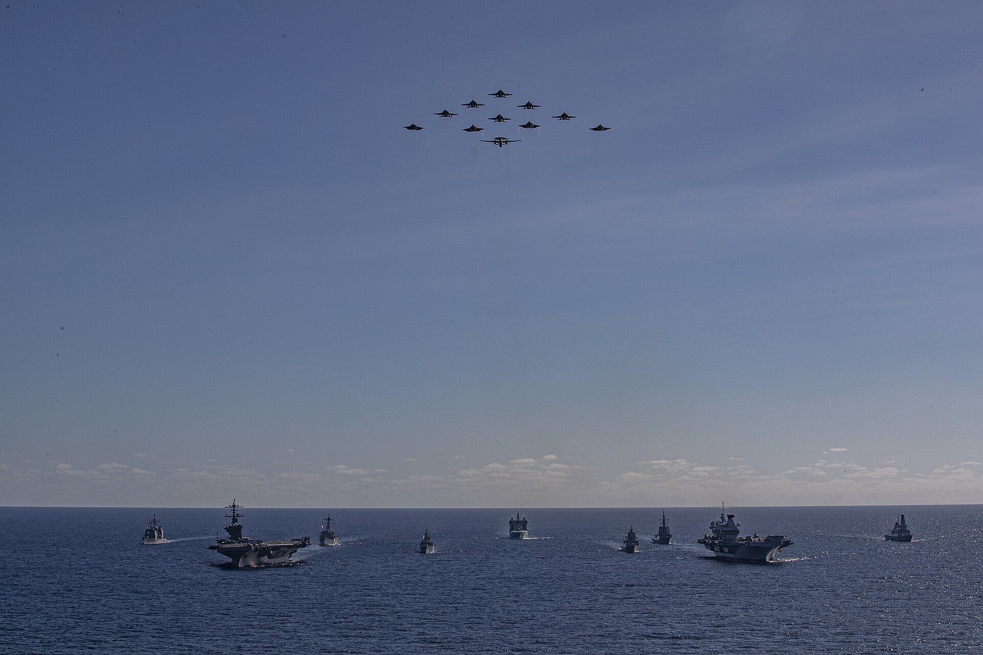 US Navy and Royal Navy carrier strike groups in formation during Talisman Sabre 2025, with aircraft flying overhead — the multi-carrier force concept now deployed to the Middle East for the first time since 2003.