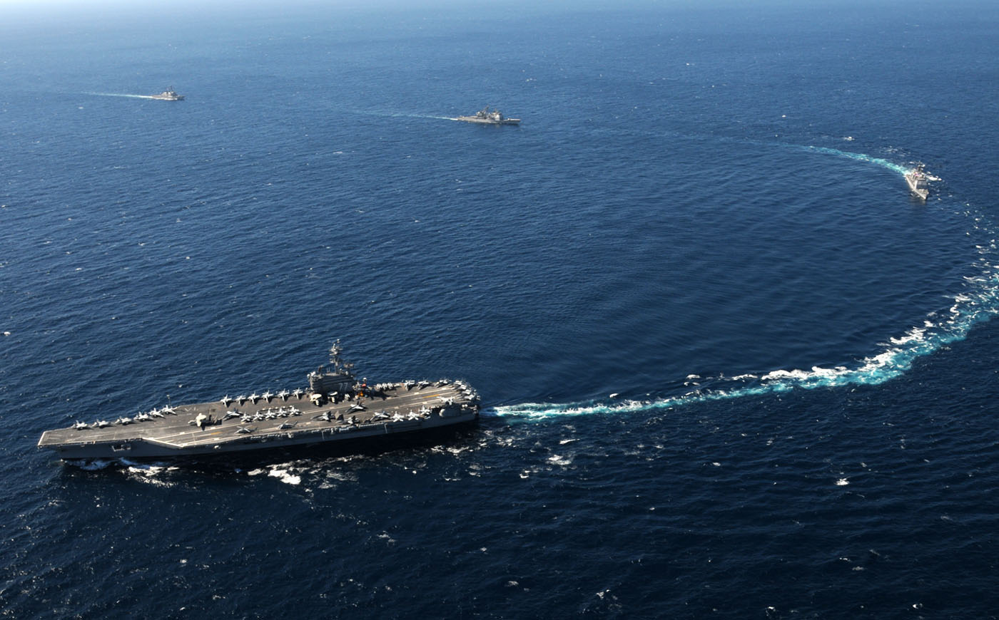 USS George H.W. Bush (CVN-77) leads its carrier strike group at sea — the escort destroyers visible in formation represent the type of force now operating outside a closed Persian Gulf.