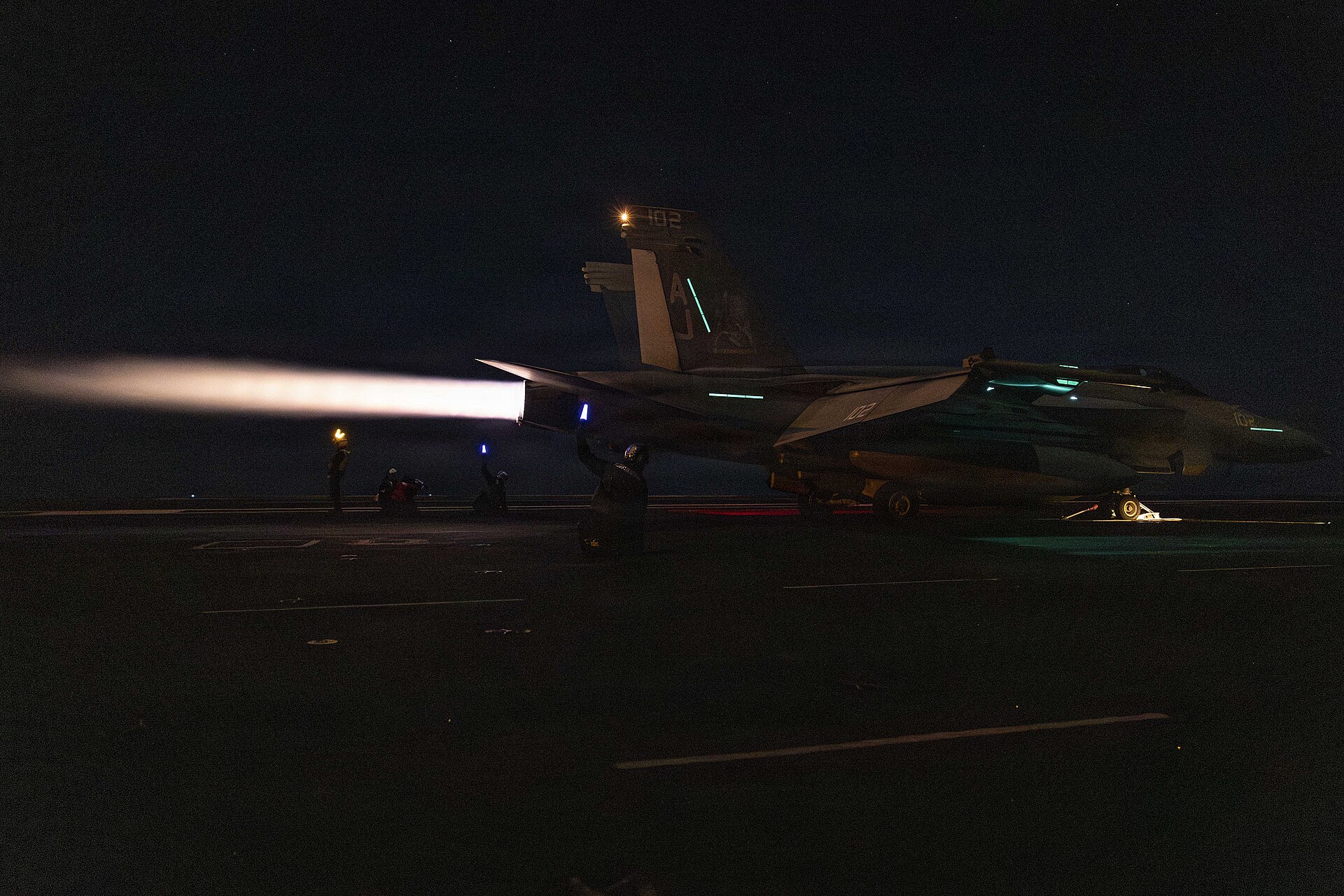 An F/A-18 Super Hornet runs up its engines in afterburner on the flight deck of USS Gerald R. Ford (CVN-78) during night operations — the Ford has been at sea for over 300 days as of April 2026.