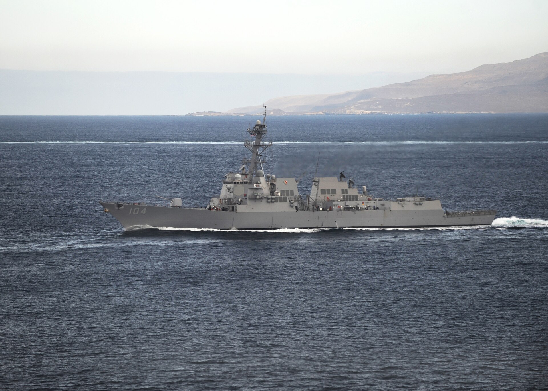 USS Sterett DDG-104 Arleigh Burke-class guided-missile destroyer underway in blue water with arid coastline in background