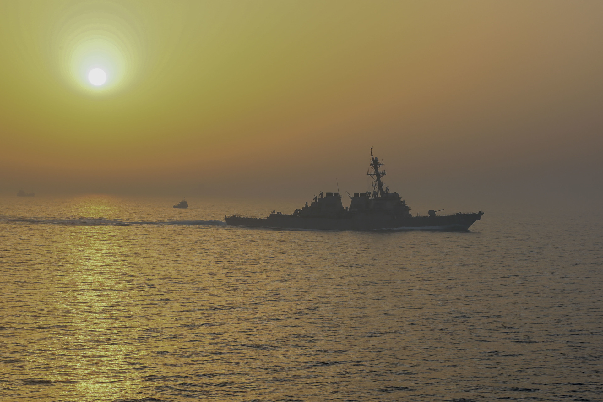 USS Stout (DDG-55) guided-missile destroyer transiting the Strait of Hormuz at sunset, with additional vessels visible in the distance
