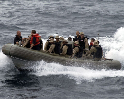 US Navy VBSS team in rigid-hull inflatable boat races toward merchant vessel for maritime interdiction boarding operation