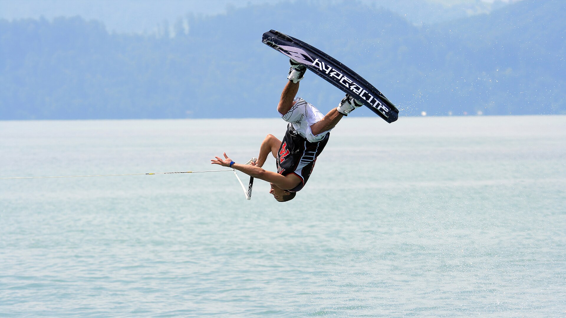 A wakeboarder performing an inverted aerial trick above calm water