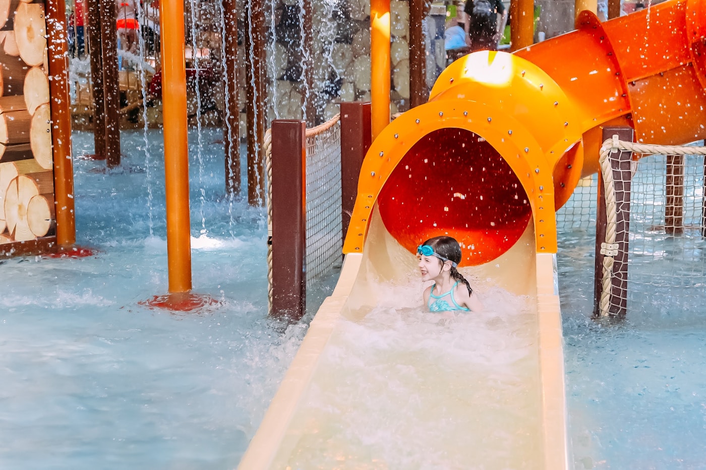 A child splashes out of an orange tube water slide at a modern water park