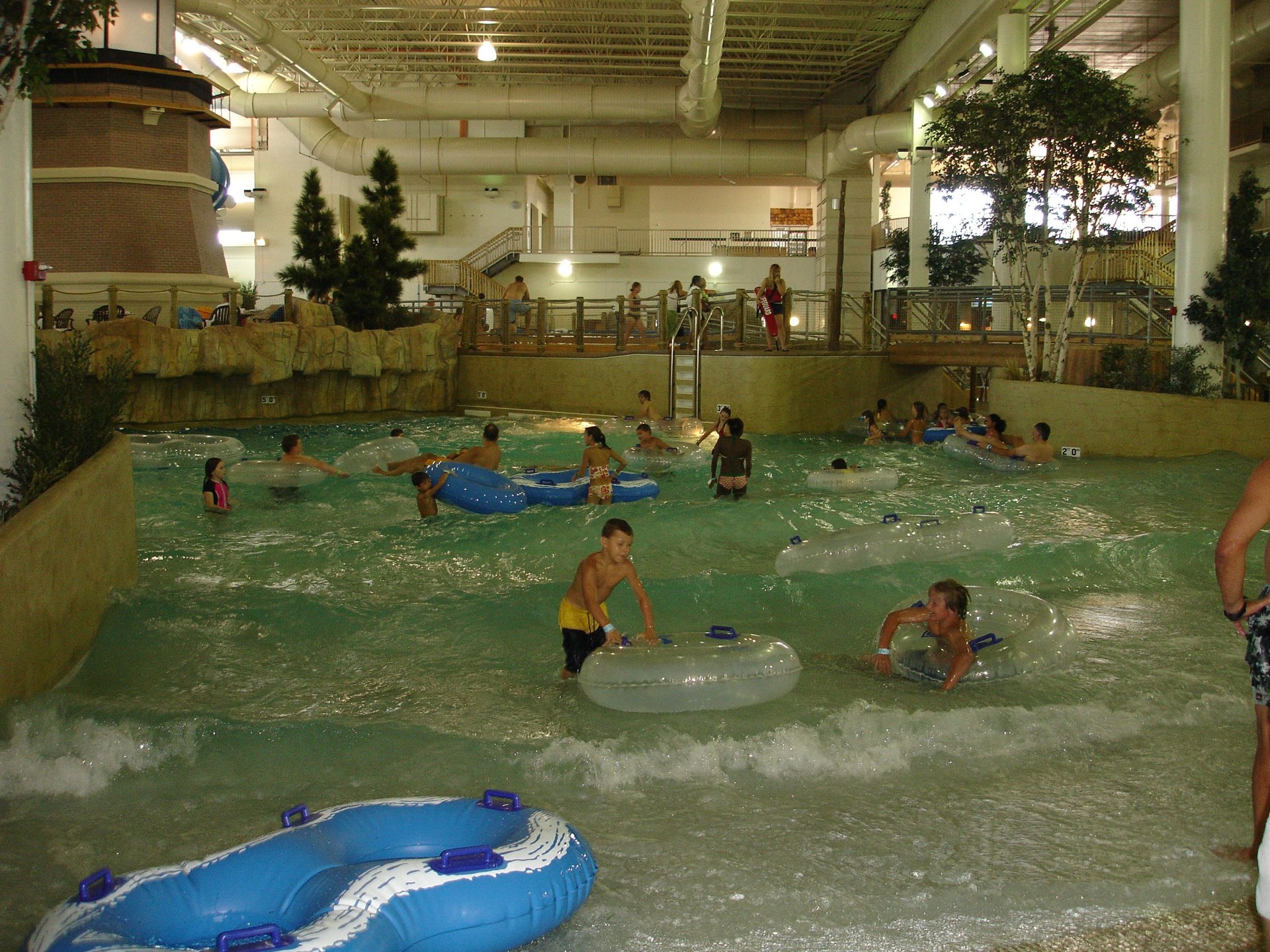 Visitors enjoying a wave pool at a water park, floating on blue tubes in churning water