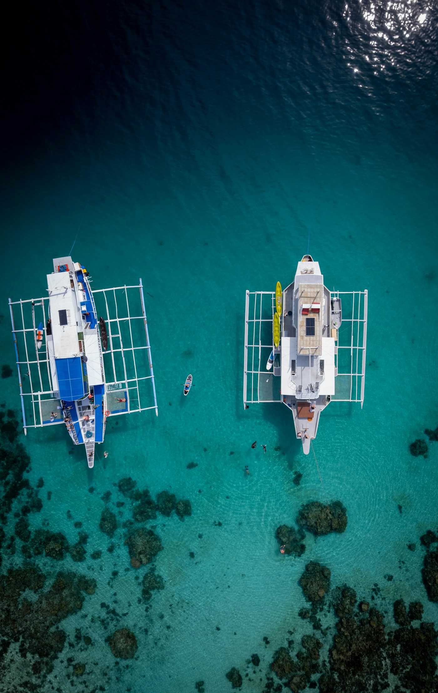 Aerial view of two charter boats anchored in turquoise water above a coral reef